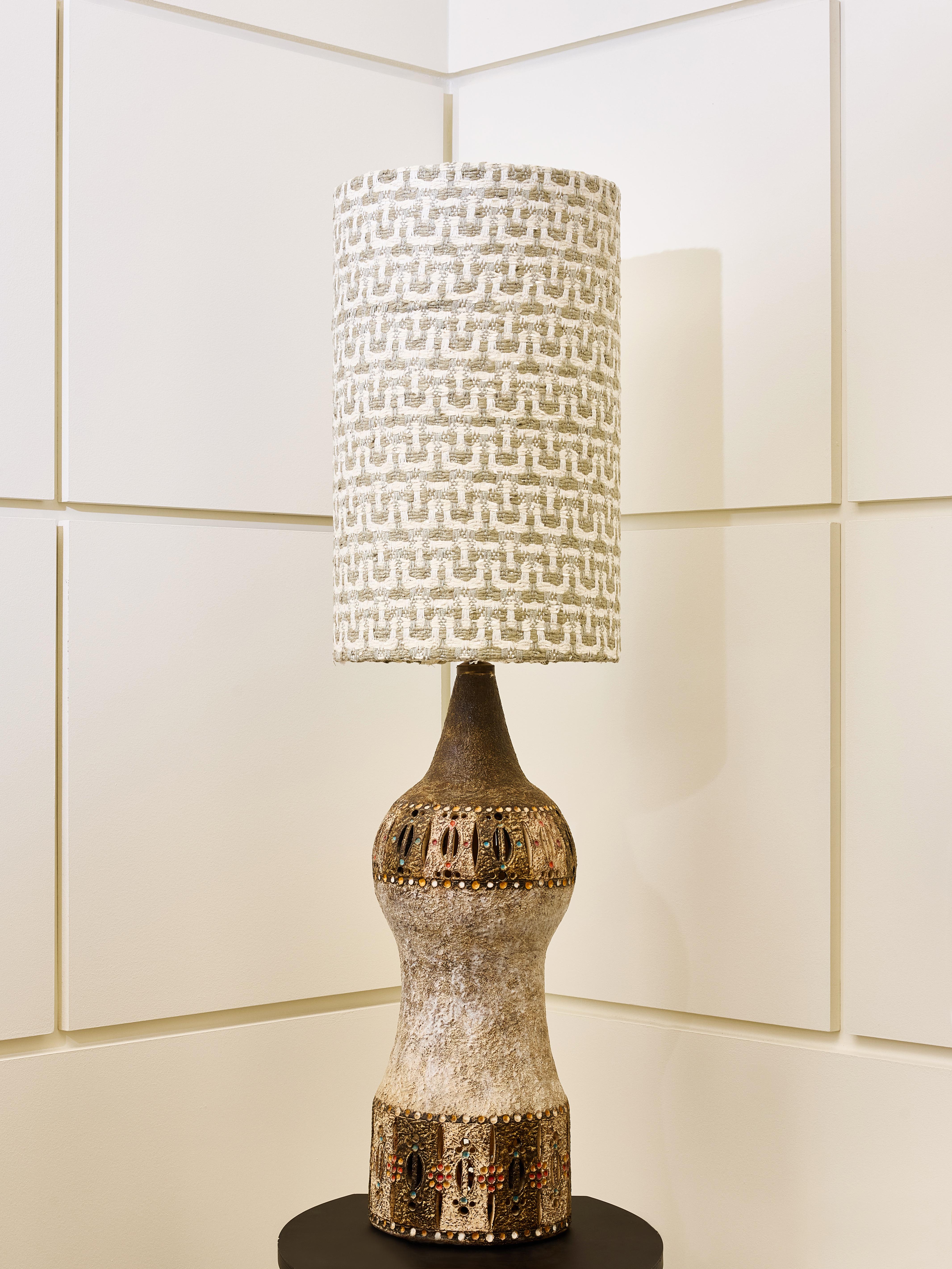 Diese Tischleuchte ist ein skulpturales Keramikstück mit einer erdigen, organischen Form, die sich in der Mitte nach innen wölbt. Der obere und untere Teil ist mit einem dekorativen Band versehen, das mit komplizierten Mustern in Gold-, Bronze-,