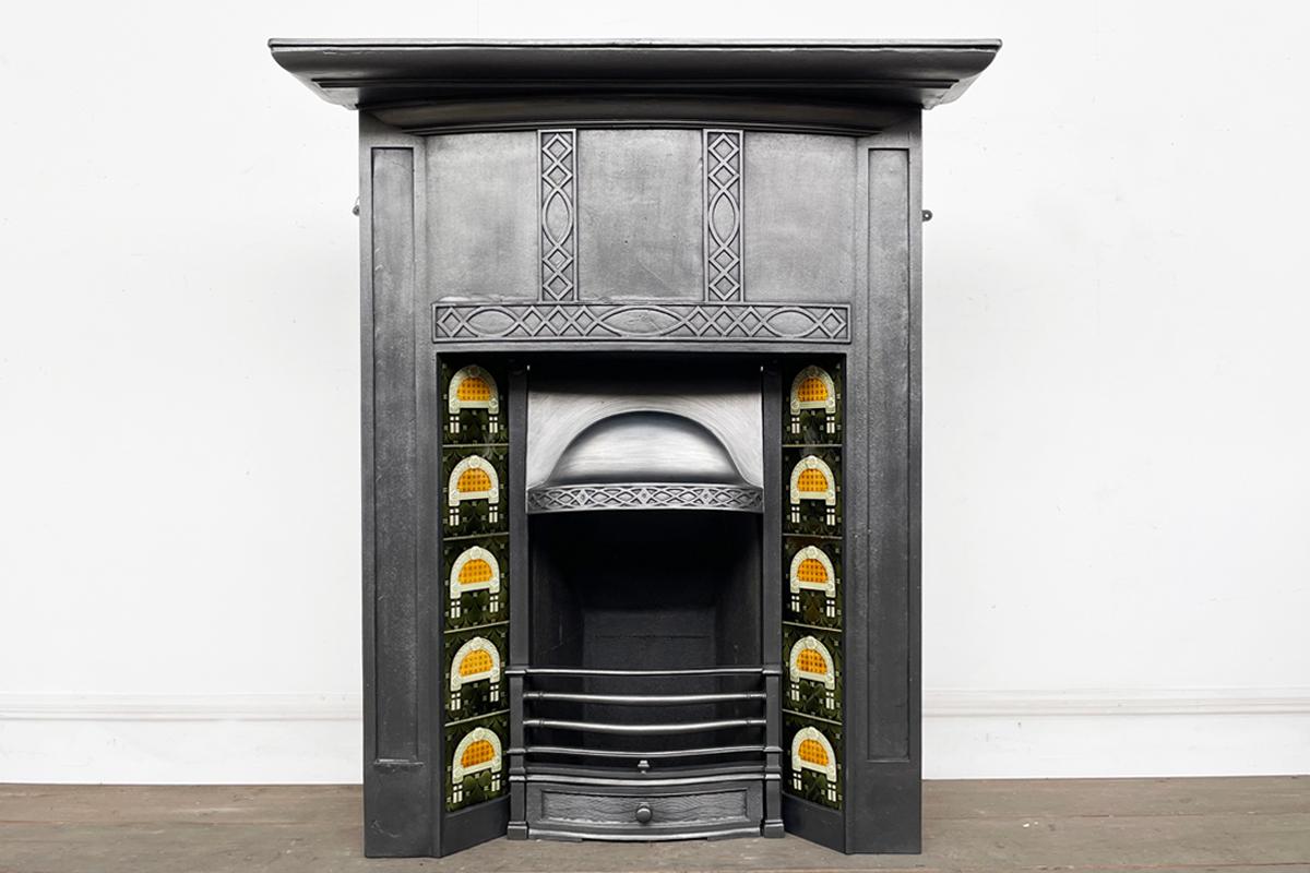 Tall reclaimed early 20th century cast iron combination fireplace. The bow-fronted frieze is decorated with blind fret detail. The same detail is found on the domed and adjustable canopy. Circa 1920.

Complete with a set of original fireplace tiles