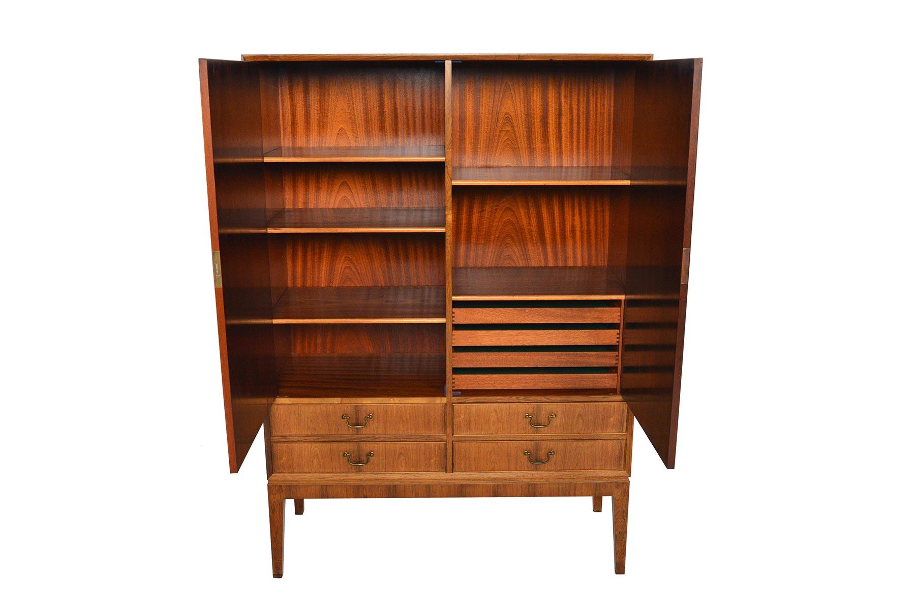 This tall Danish modern bureau is crafted in Brazilian rosewood and offers a beautiful sun- patinated finish. Two large locking doors open to two bays with adjustable shelves and drawers. Four lower drawers with brass pulls provide additional