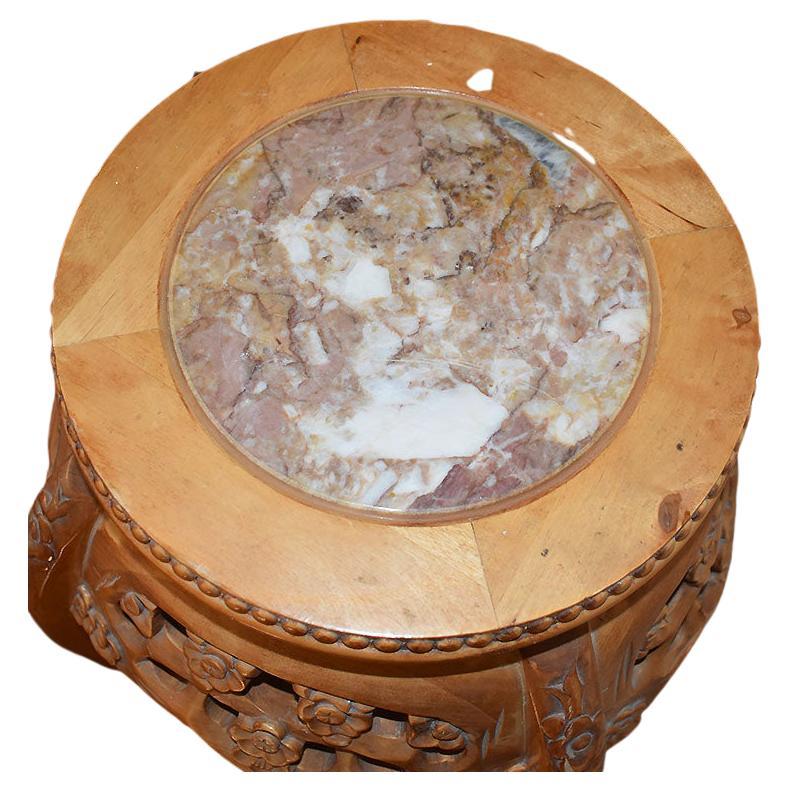 A chinoiserie hand-carved wood plant stand, with a circular pink marble top. This piece would be great for use as a plant stand, a tall side table or to display a sculpture. The piece has a round top and is decorated around the sides with an
