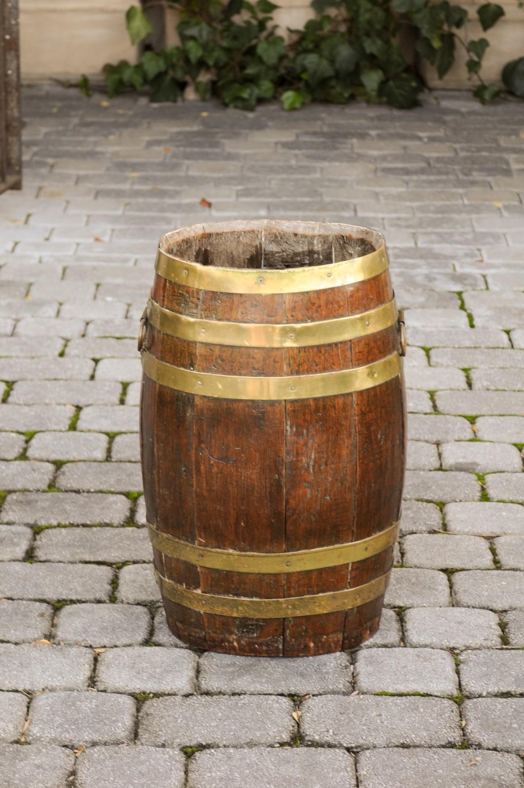 A tall English oak barrel from the late 19th century, with brass braces. Born in England during the later years of the 19th century, this tall barrel presents an oval shape made of thin vertical slats, reinforced by the presence of brass braces,