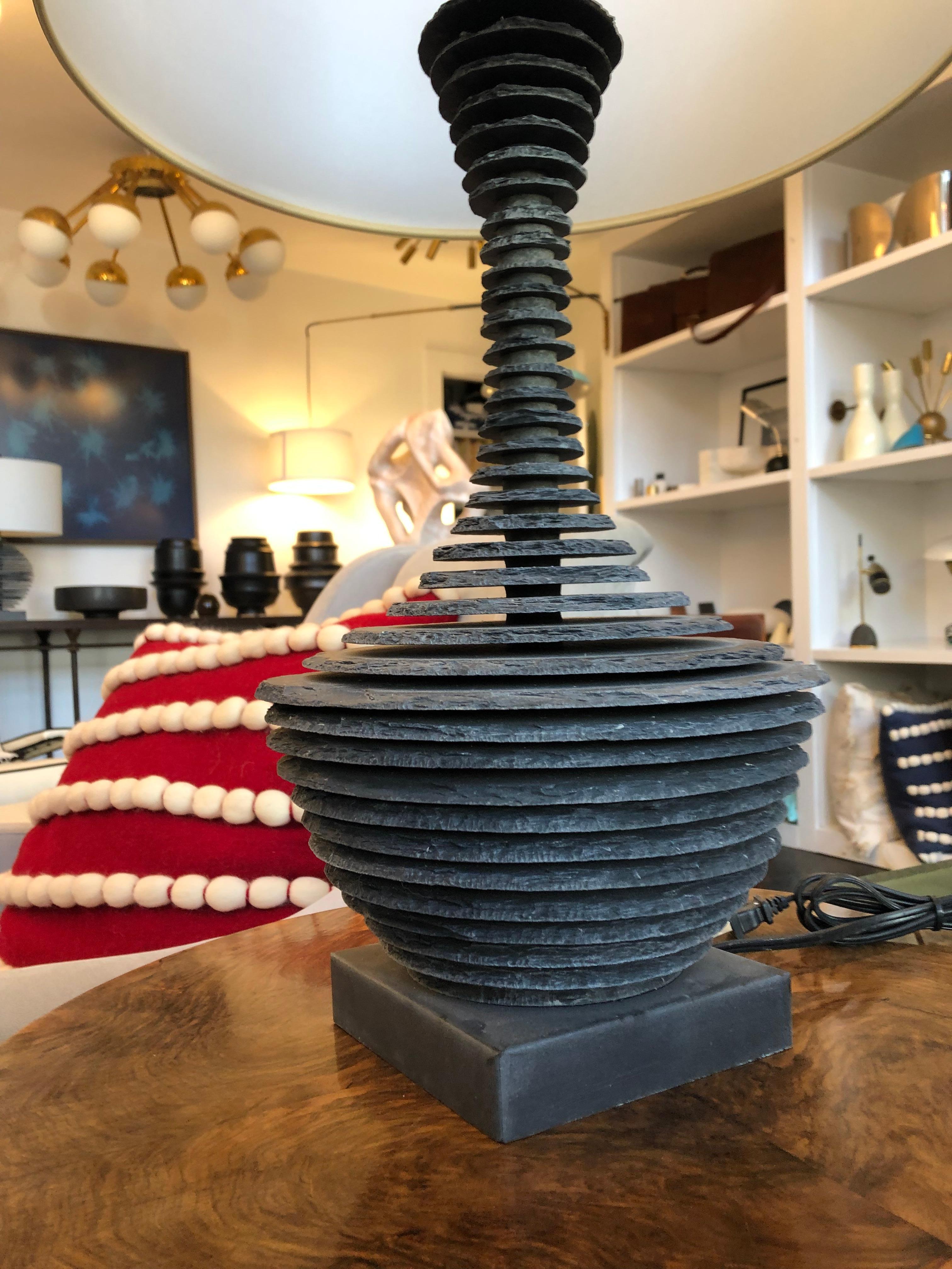 The lamp base is hand crafted with multiple individually carved sections of blue stone slate, then with mathematical precision is hand layered in horizontal parallel sections leaving space between each section creating an optic see through illusion.