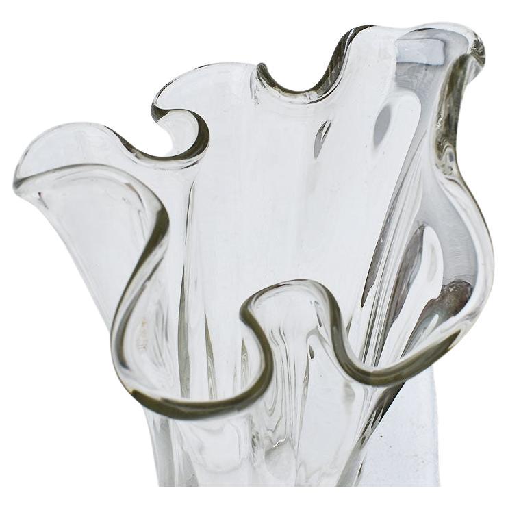 Un grand vase sculptural en verre transparent avec des bords volantés. La base de cette beauté est ronde, avec des bords festonnés. Le corps a de longs bords arrondis qui se graduent et s'enroulent vers l'extérieur à des hauteurs alternées.