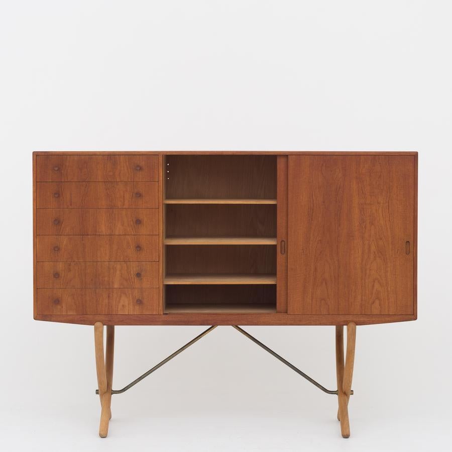 CH 304, sideboard in teak with oak cross-leg frame and brass hangers. Front with six drawers and two sliding doors. Maker Carl Hansen.