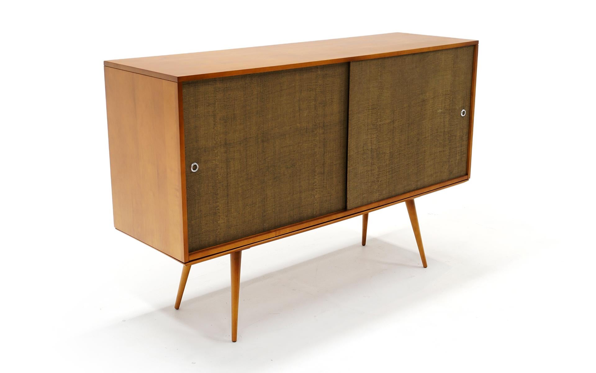 Paul McCobb Planner Group credenza / buffet for Winchendon. Measures: 39 inches tall. Made of solid birch with original grasscloth / grass cloth sliding doors which reveal multiple drawers, shelves and storage spaces. The cabinet sits on a 15 inch