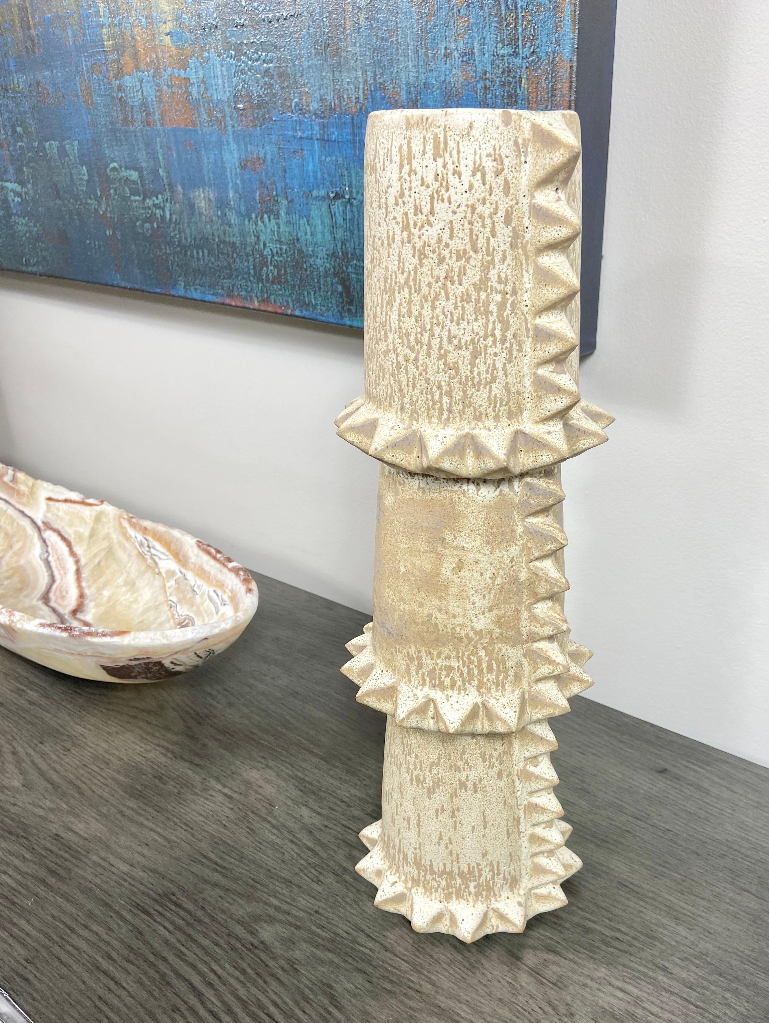 A tall ceramic stacked totem-like vase by Los Angeles based LGS Studio. This one of a kind hand-made piece features a mottled glaze from off white to light mocha. It is meticulously hand carved with ceramic spikes. This vessel stands alone