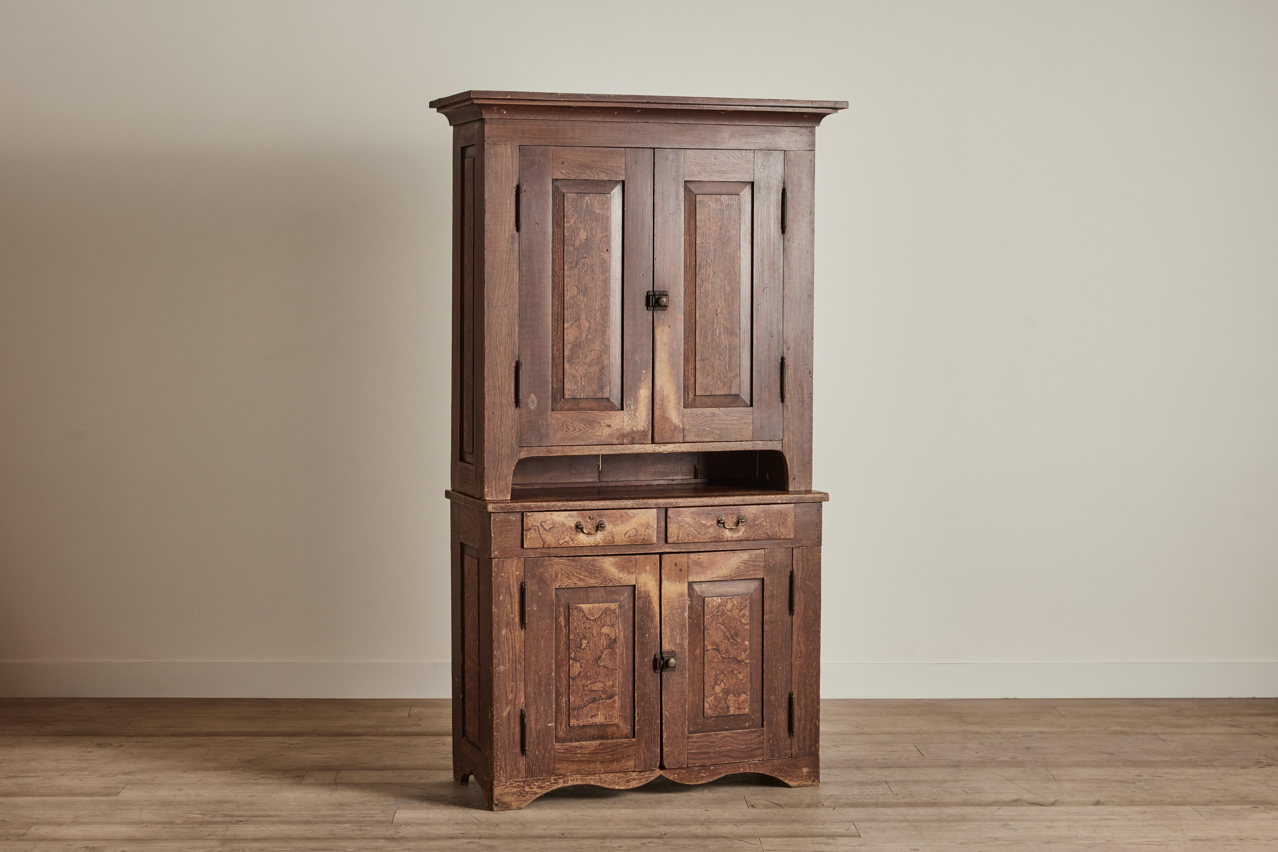 Tall nineteenth century step back cupboard with worn grain painted finish. This piece has a large upper compartment with shelving, two counter height drawer, and a lower compartment for generous storage. Cupboard has visible wear throughout that is