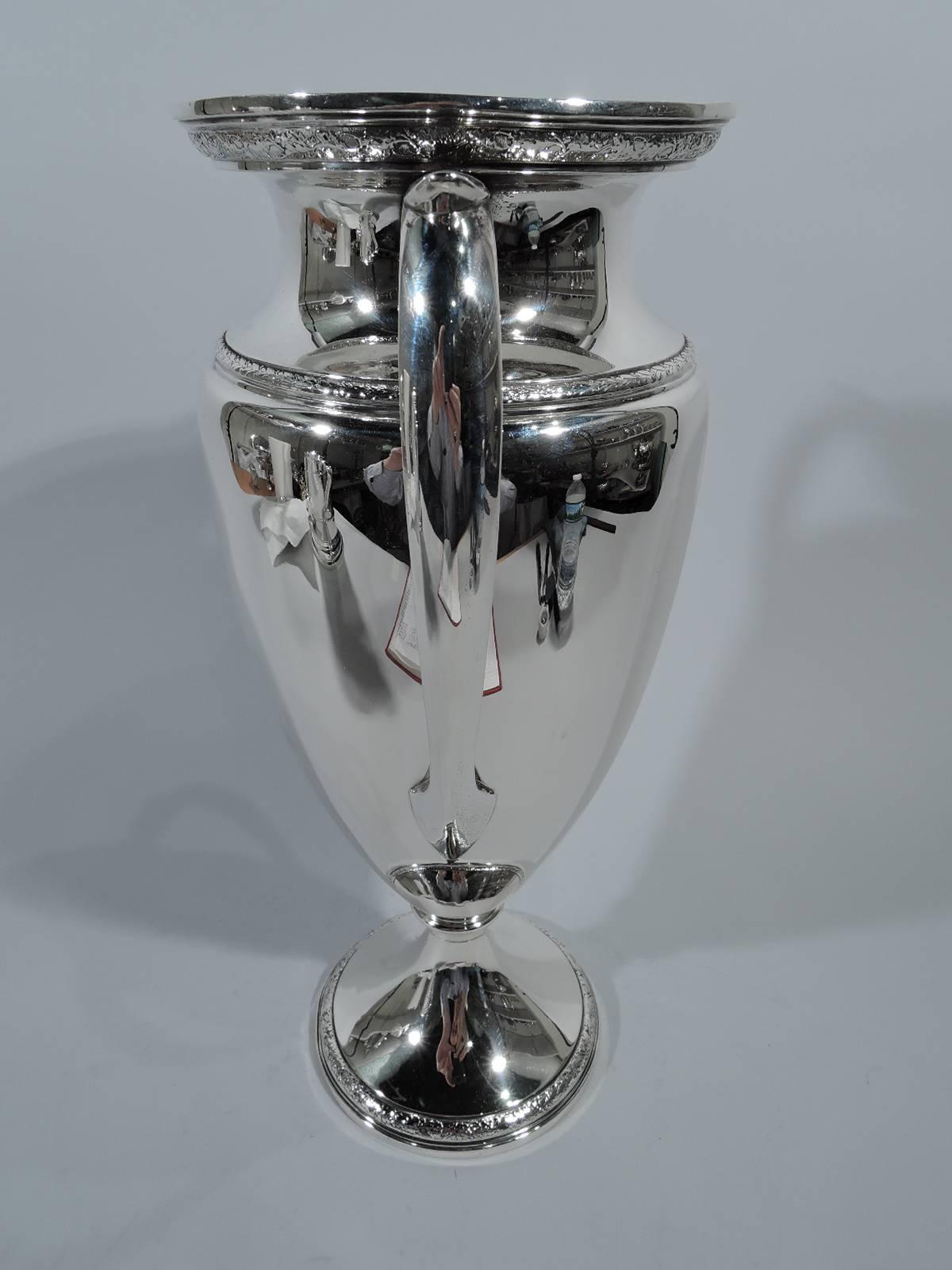Tall sterling silver trophy cup. Made by Gorham in Providence in 1930. Amphora with capped side handles and raised foot. Bands of leaf ornament on rim, shoulder, and foot. Hallmark includes date symbol and no. A12843. Weight: 26.4 troy ounces.