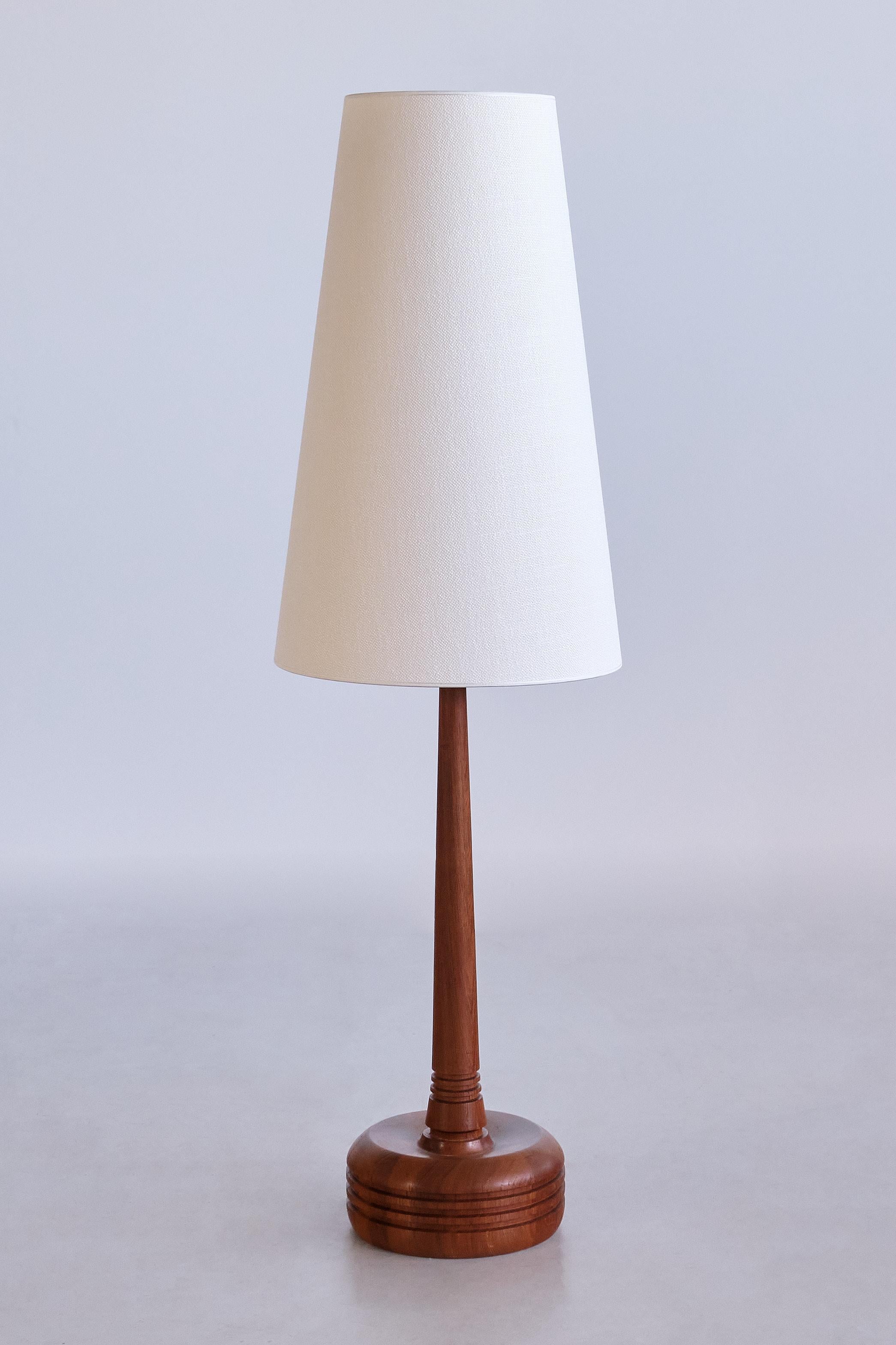 This rare tall table lamp was produced by Tranås Stilarmatur AB in Sweden in the 1960s. The lamp is marked with the manufacturer's sticker next to the bulb holders.
Made of solid teak wood, the circular base and tapered central stem both have three