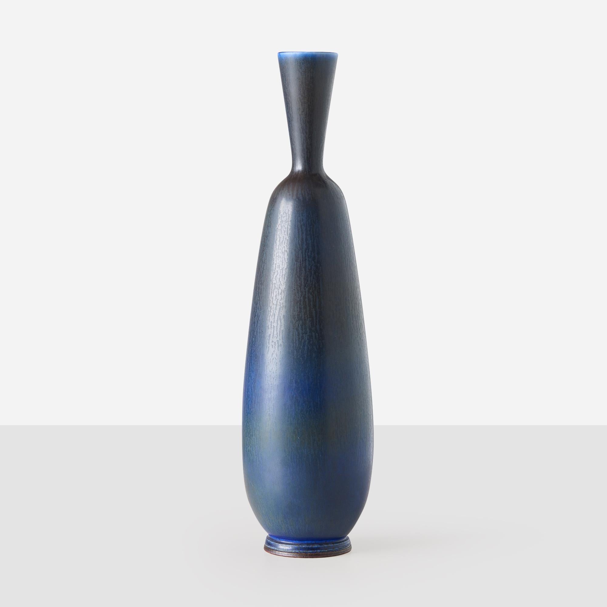 Ce vase en grès tourné par Berndt Friberg présente un col mince et allongé et une glaçure lisse dans des tons de bleus et de gris profonds. Il illustre le savoir-faire raffiné et la forme élégante d'Eleg. Le dessous est gravé de l'inscription
