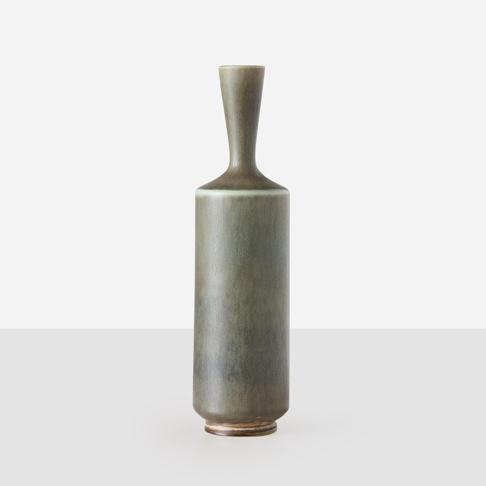 Ce vase en grès tourné par Berndt Friberg présente un col mince et allongé et une glaçure lisse dans des teintes d'olives et de gris audacieux. Il illustre le savoir-faire raffiné et la forme élégante d'Eleg. Le dessous est gravé de l'inscription