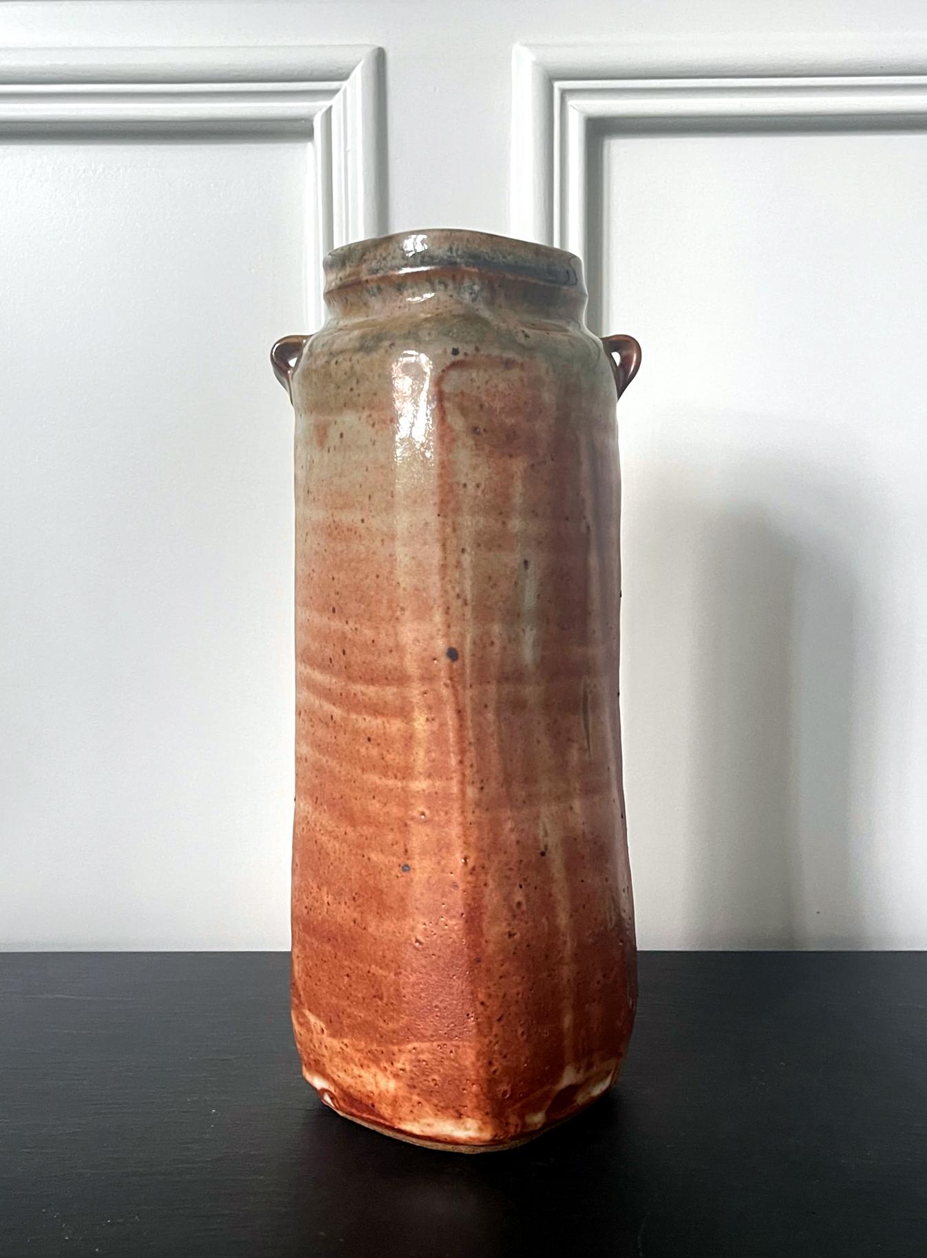 Un grand vase en grès de forme cylindrique du potier américain Warren MacKenzie (1924-2018). Le vase présente une forme légèrement ambiguë entre le cercle et le carré et il comporte deux petites boucles sur l'épaule. La surface est recouverte d'une