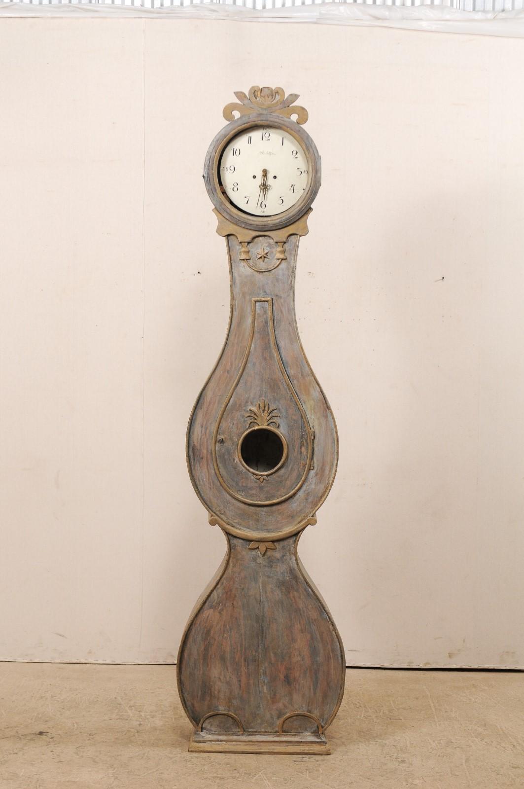 A tall Swedish Fryksdahl floor clock from the 19th century. This Fryksdahl clock from Sweden showcases ornamental carvings throughout, which enhance and accentuate this shapely clock. The crest or crown features a pierced carving in foliage inspired
