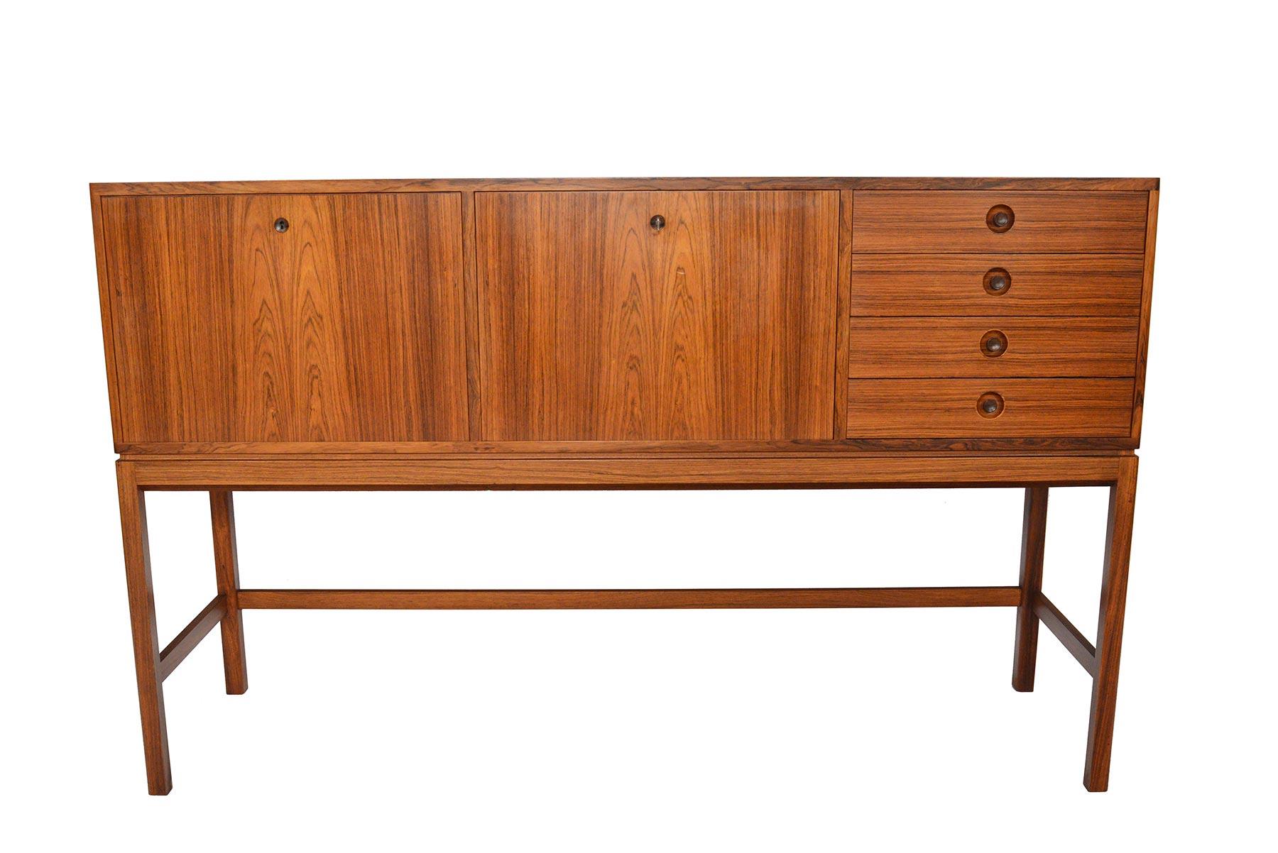 Standing on tall sculpted legs, the silhouette of this Swedish modern credenza is unlike any other. Beautifully detailed, emphasis is directed on distinguished wood grain. Each locking cabinet is adorned with a recessed rosewood escutcheon. The left