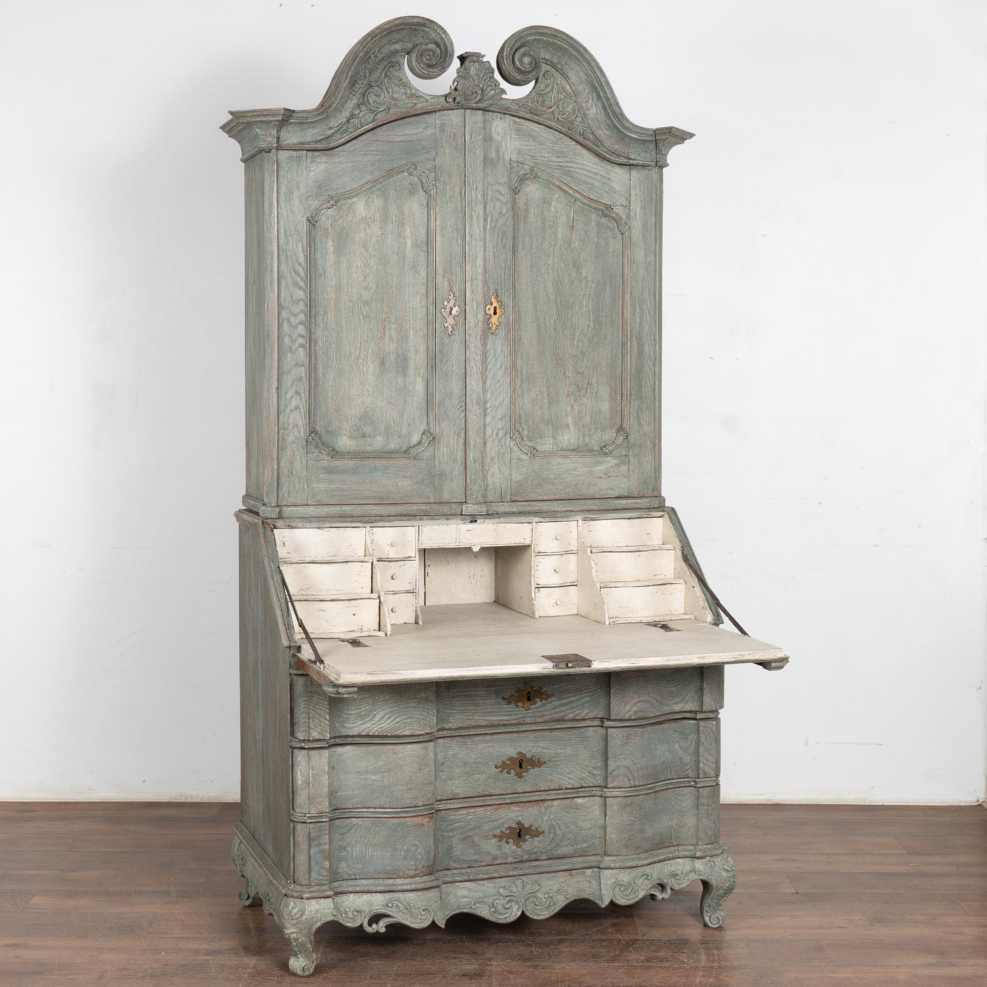 This striking oak secretary is an elegant statement piece crowned with an elaborate carved pediment and decorative skirt.
The secretary has been given a professional custom teal green/blue layered/striated painted finish which has been gently