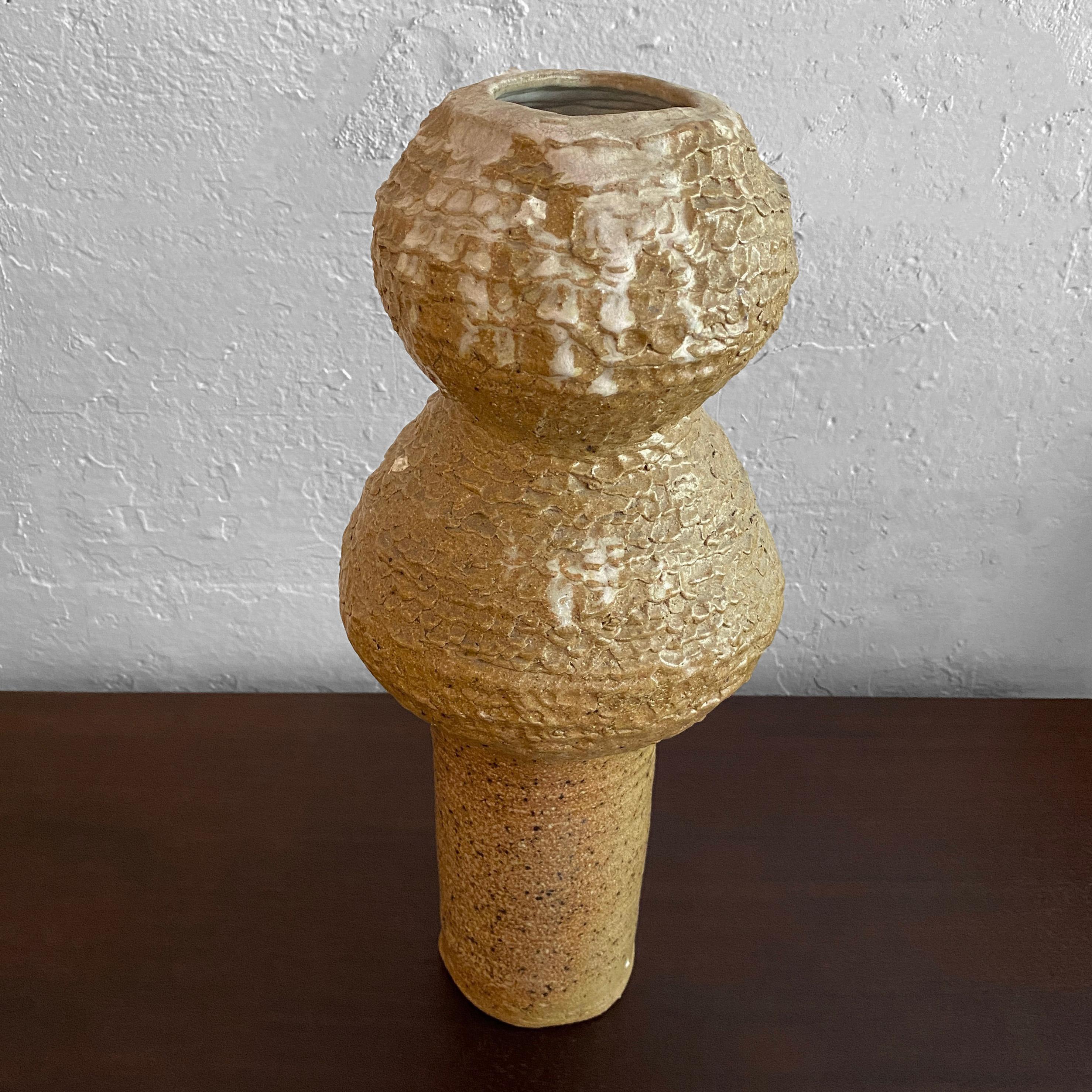 Interesting, tall, tan, brutalist art pottery vase features an organic shape with rough-hewn, brutalist texture. The mouth opening measures 2.5 inches diameter.