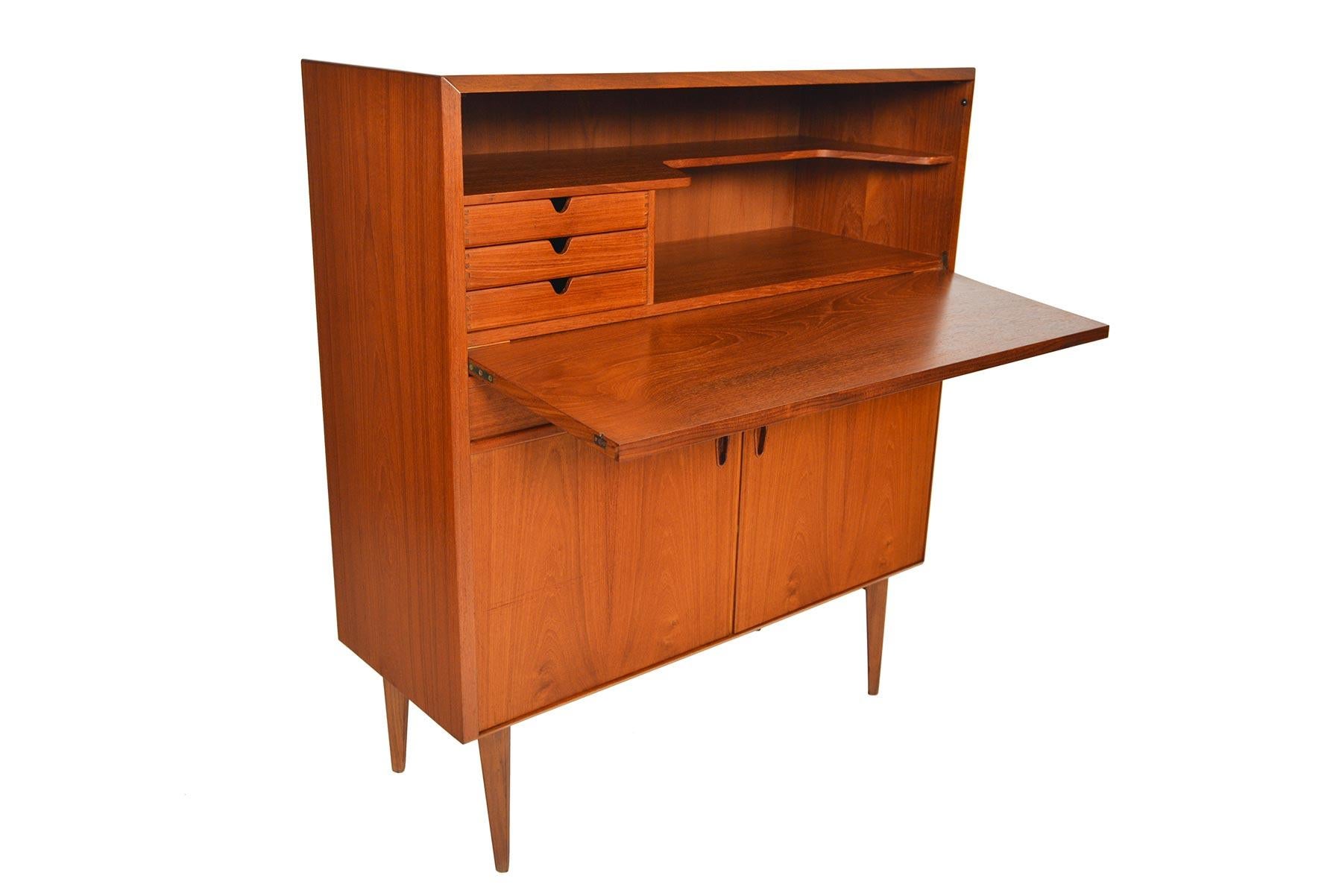 This wonderful Mid-Century Modern dry bar in teak was designed by Arne Wahl Iversen in the 1960s. A large teak door drops to expose three drawers and a carved fixed shelf. Two drawers sit in the middle. Two lower doors open onto two bays with