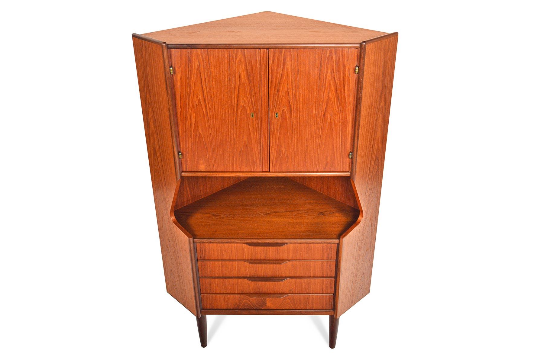 This Danish modern midcentury corner unit offers a tall teak design perfect for storage and display. The top cabinet unlocks to reveal a mirror lined bar with rosewood shelves. Beneath is a cubby and four small drawers. In excellent original