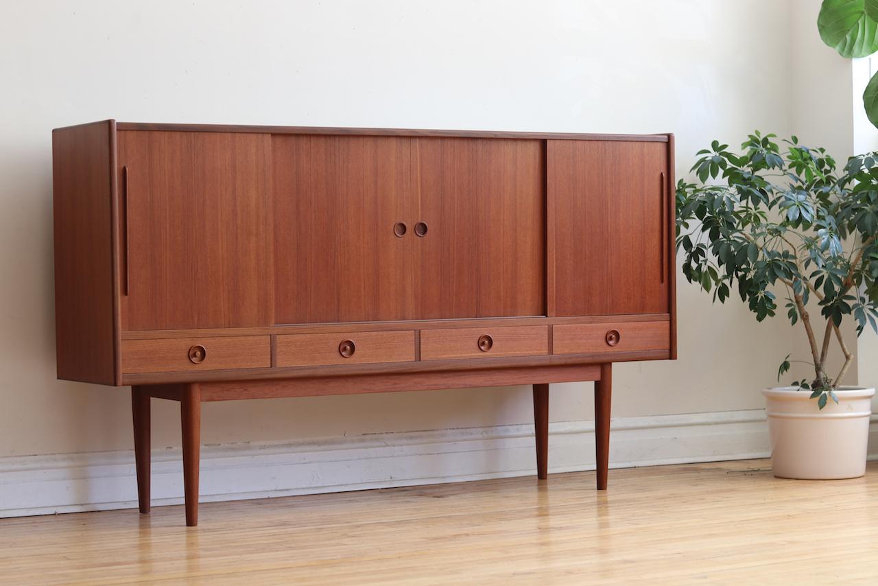 Mid-Century Modern Danish tall teak wood credenza.
Just imported from Copenhagen!
Minimal style with sculptural handles and lovely teak woodgrain.
Adjustable shelving.
Four dovetailed drawers below cabinets.
Three additional hidden drawers with