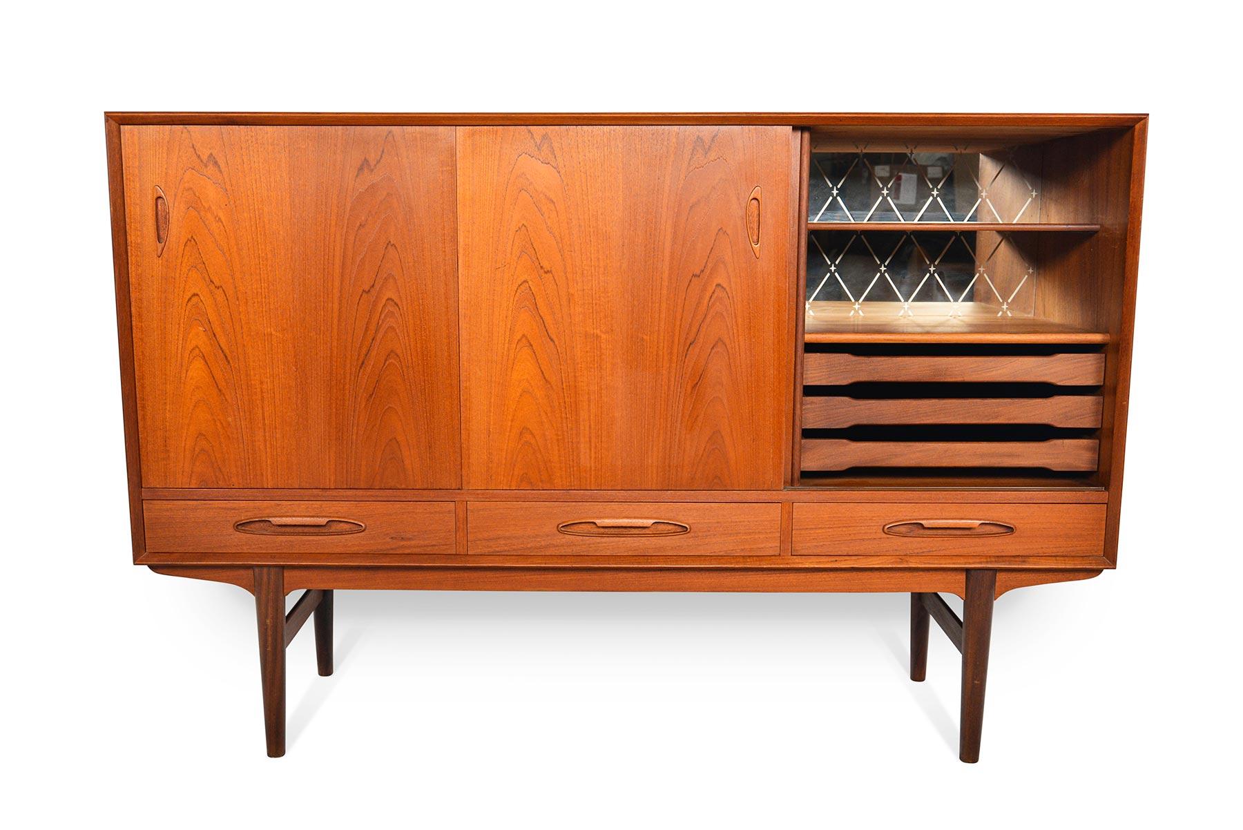 This fantastic Danish modern tall teak credenza offers a solution for organization, storage, and entertaining! This stunning storage piece offers two bays. The left oriented bay offers two adjustable shelves. The right bay features an original