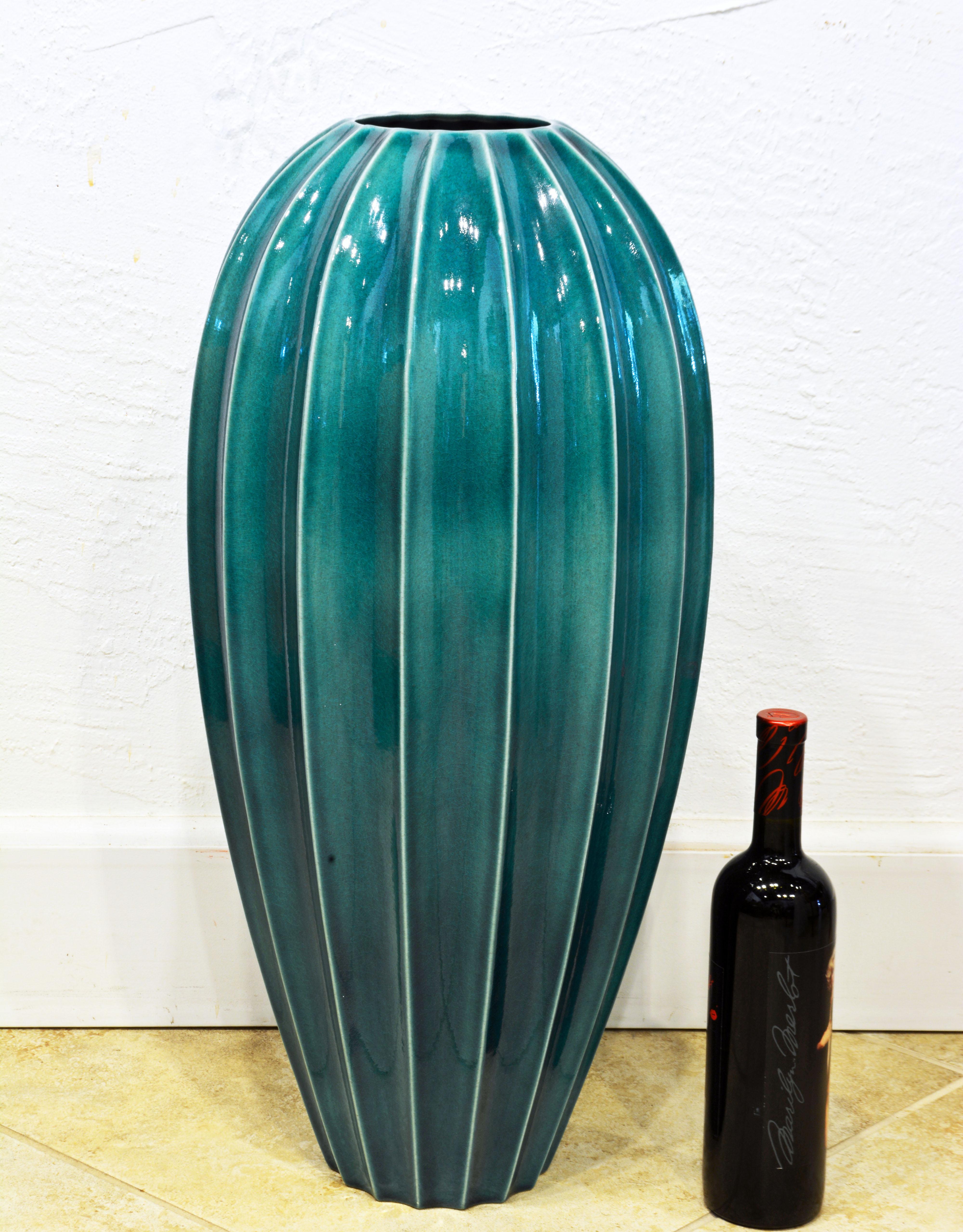 Standing 26 inches tall this Oggetti floor vase is the epitome of timeless design. The color of the glaze fluctuates between malachite green and turquoise divided by the light cream edges of the ribs. The vase is great on the floor but its