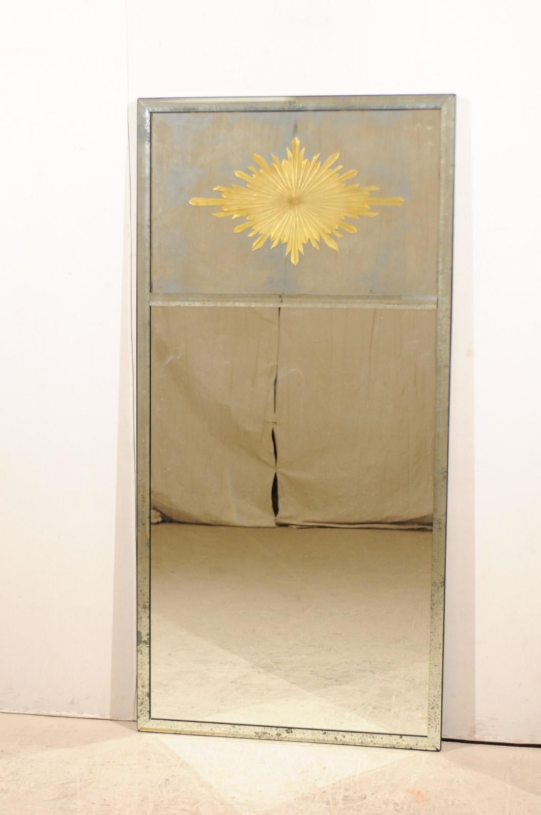 A tall American mirror with verre églomisé sunburst at upper center within a mirrored frame. This rectangular-shaped mirror stands at over 6.25 feet tall, features a cleanly designed antiqued-mirror surround, two-paneled glass center, with the gold
