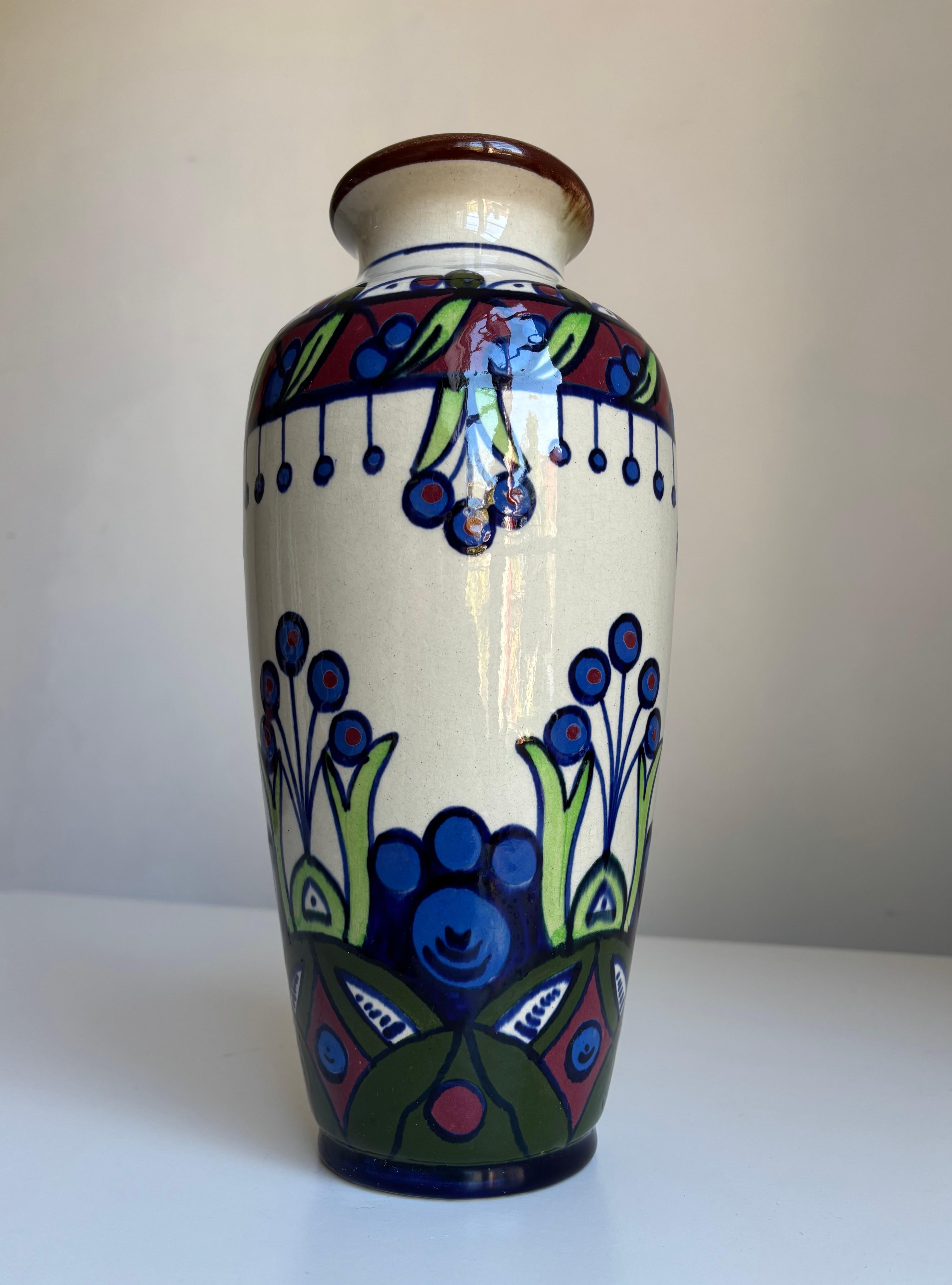 Vaso alto in ceramica belga con smalto bianco caldo, spesso e lucido e decorazioni organiche stilizzate dai colori vivaci. Blu indaco, rosso bordeaux, verde mela e verde bosco.
Timbrata, firmata e numerata sotto la base. 
Bellissime condizioni