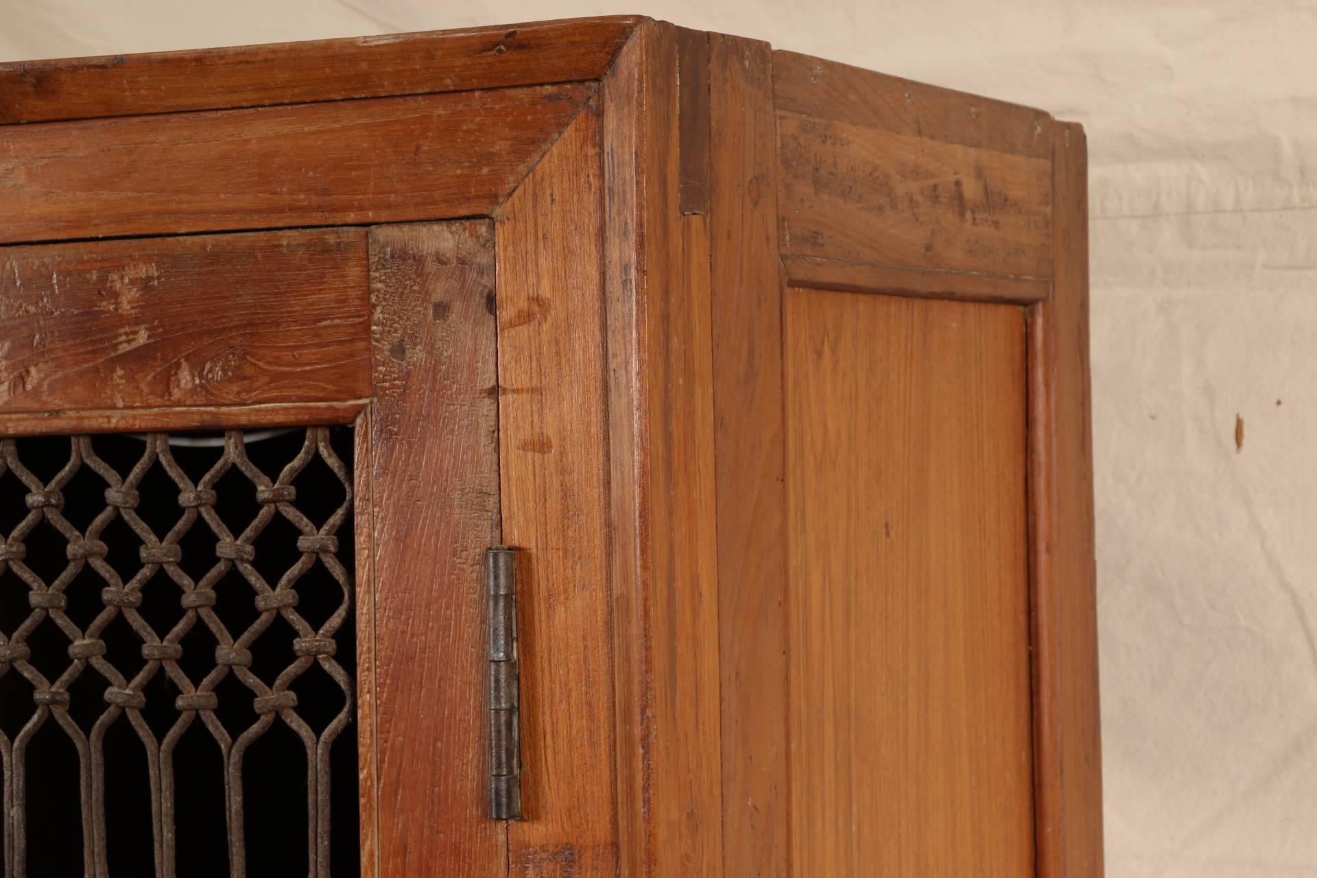 Wood storage cabinet with three shelves and tripartite sectioned door with iron grille work. A shaped apron all around, dowel construction.
Condition: very good with rust patina to the grilles, worn finish to the apron.