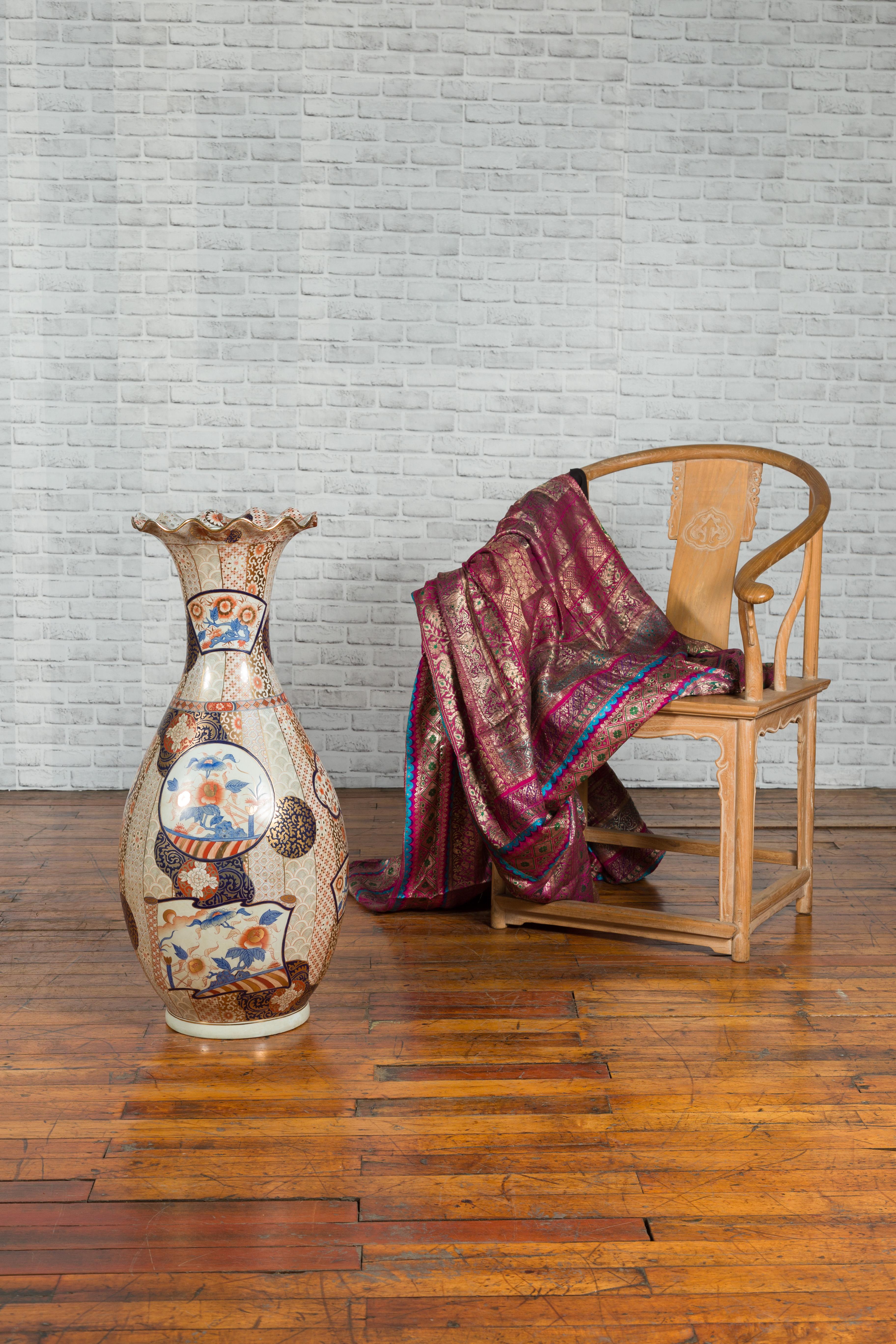 A vintage Chinese tall vase from the mid-20th century, with hand painted decor. Created in China during the midcentury period, this tall vase features a scalloping lip with gilt edge, sitting above a generous body adorned with blue, orange and