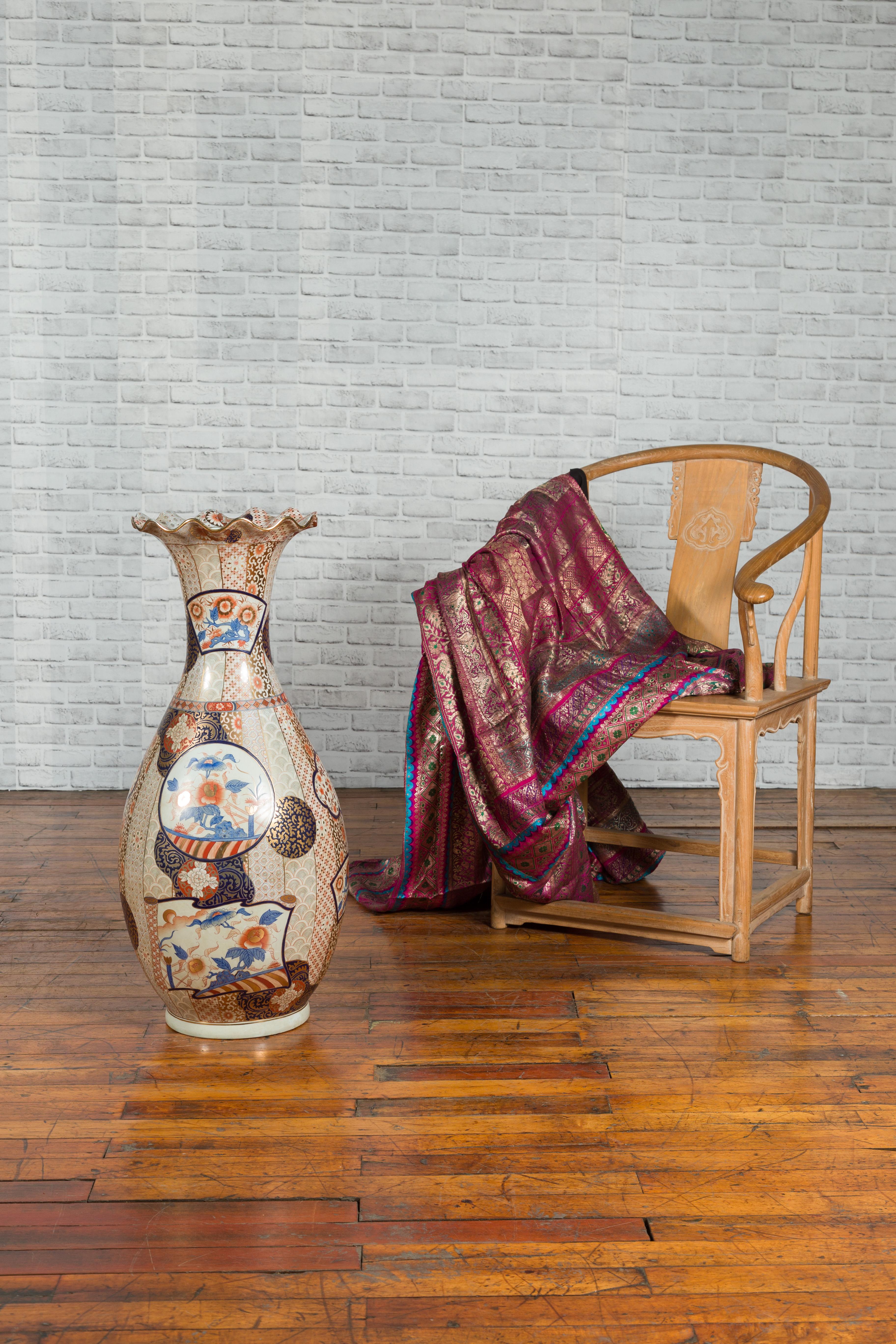 A vintage Arita Japanese style tall porcelain vase, with hand painted decor. This vintage Arita Japanese style tall vase enchants with its refined shape and exquisite hand-painted décor. Topped with a scalloping lip edged with gilt, the vase