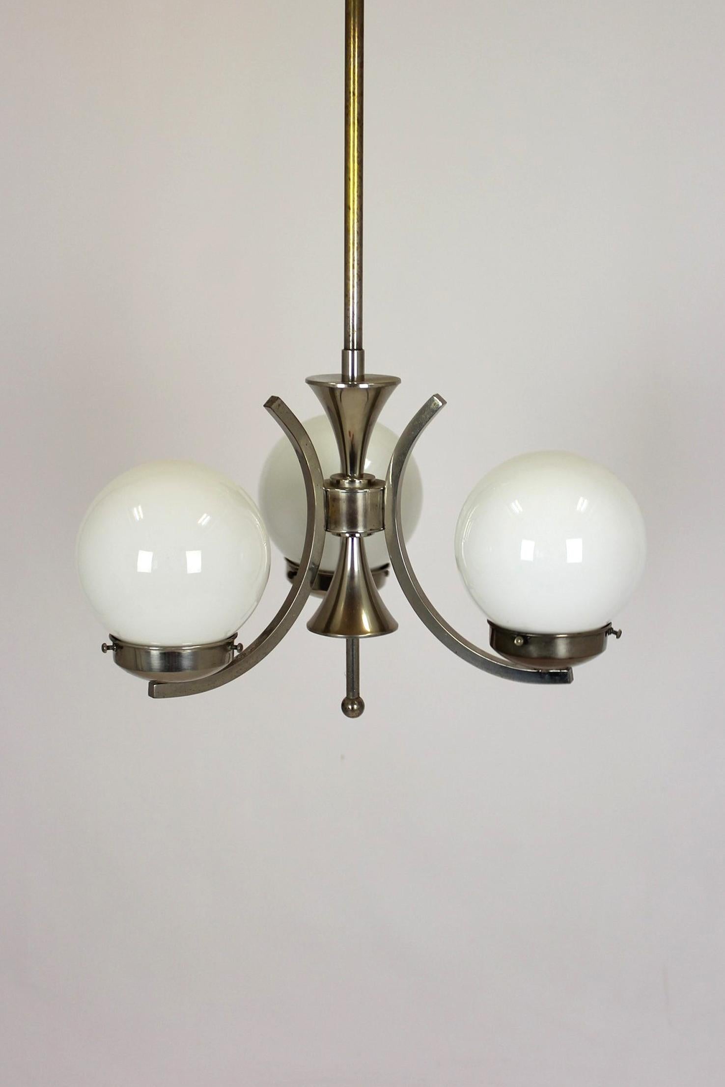 Czech pendant lamp from the 1940s, influenced by Bauhaus and functionalist design. It features three opaline glass globes mounted on curved chrome-plated metal arms. The lamp has a clean, geometric form and is made with solid materials. It remains