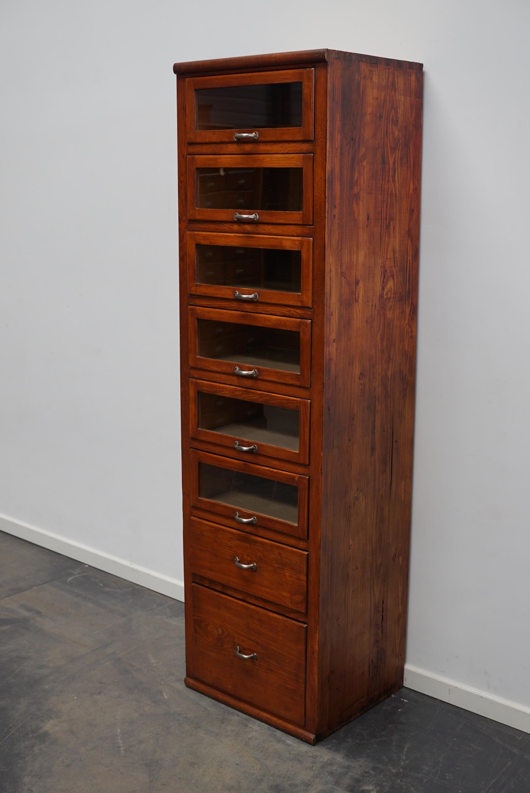 This haberdashery cabinet was produced during the 1950s in Germany. This piece features 8 drawers in pine with glass fronts and metal handles. It was originally used in a shop for sewing supplies. The interior dimensions of the glass fronted drawers
