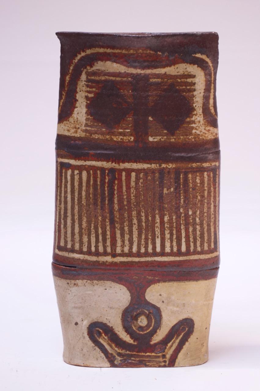 1970s tall studio pottery vase, uniquely thin with a flared top. Hand-applied linear and geometric design with an attractive color palette of brown, beige, and red. 
Unsigned, but attribute to the ceramicist, 