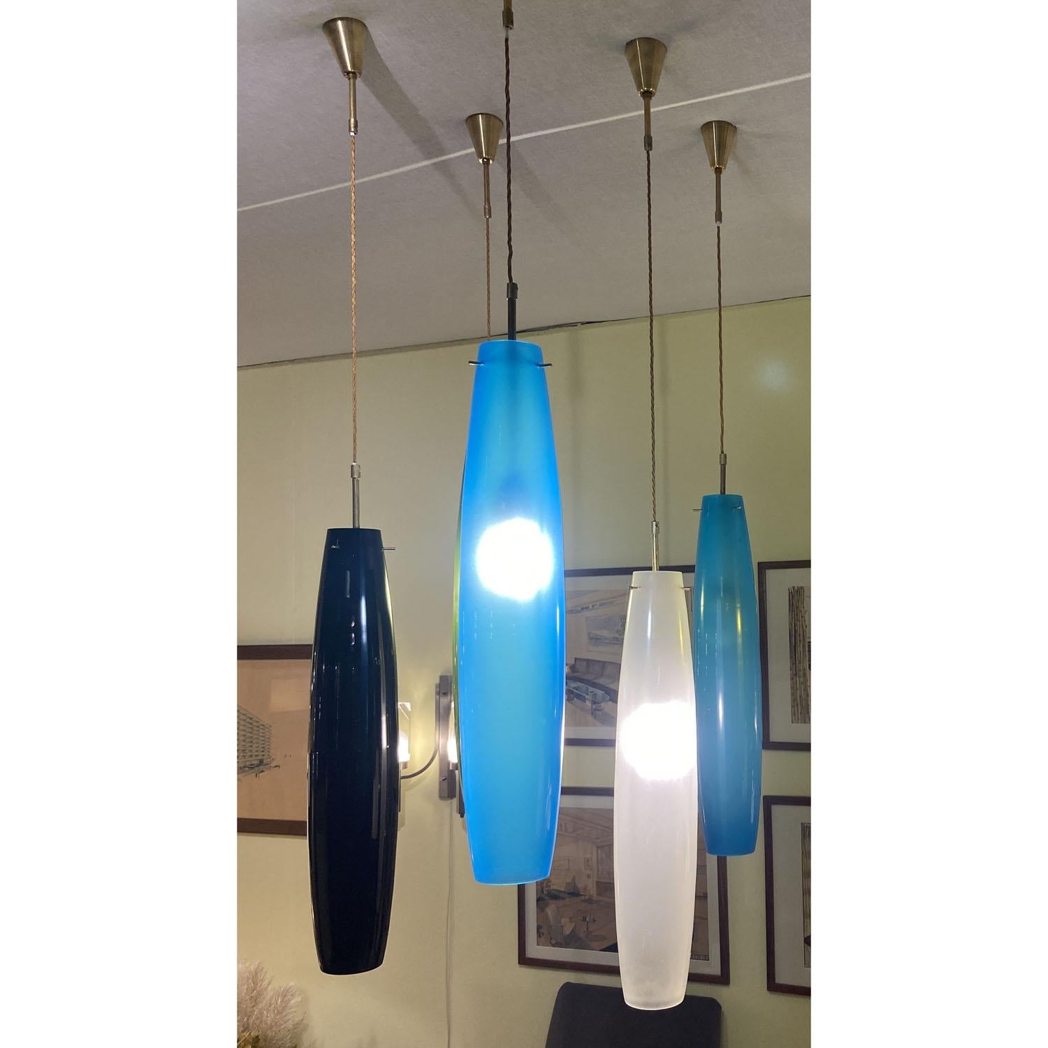Large elongated Murano blown glass pendants in blue, (Inside is a blown thin inner layer of white opal translucent glass to spread a warm and soft light) white and black. The ellipse shaped ceiling pendants are suspended by brass hanger’s holding a