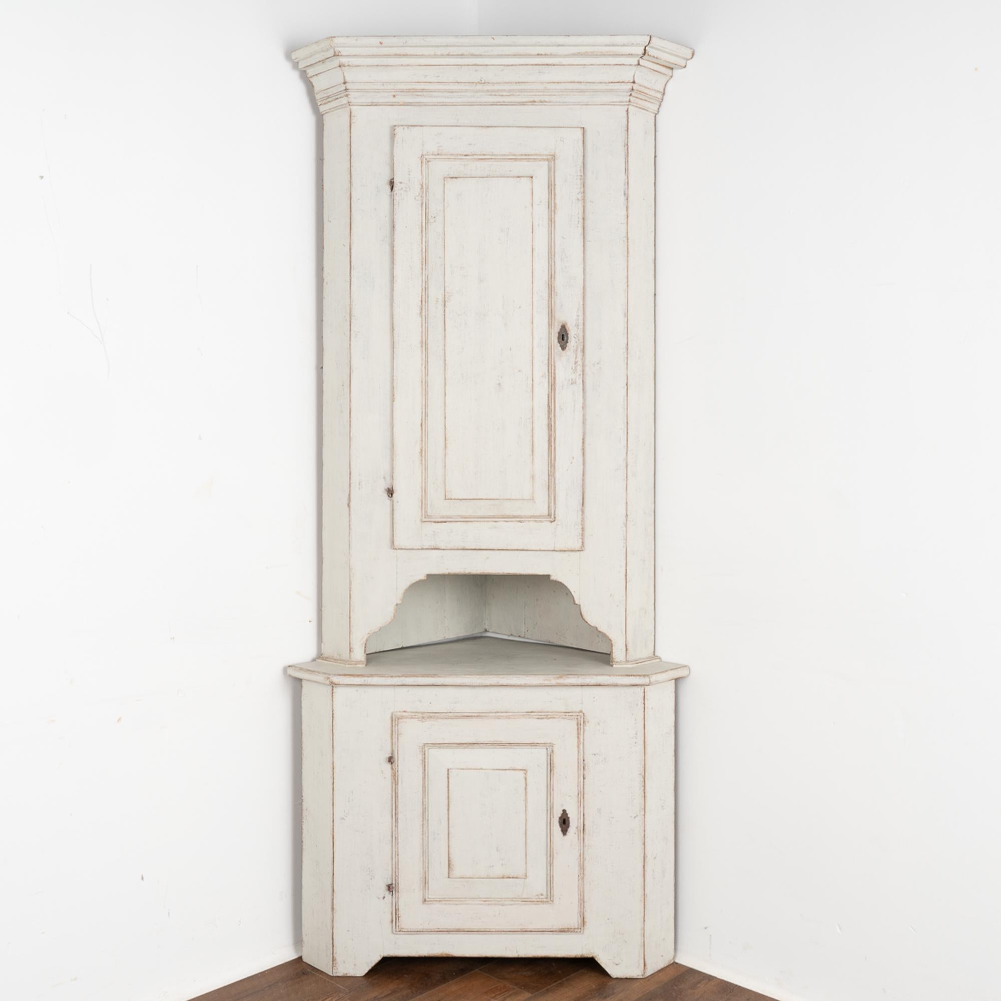 This statuesque pine corner cabinet has clean, straight lines and was crafted in the early 1800's. It is built in two sections and stands over 7' tall. 
Restored, strong and stable; later painted in layered shades of white and light gray; it is