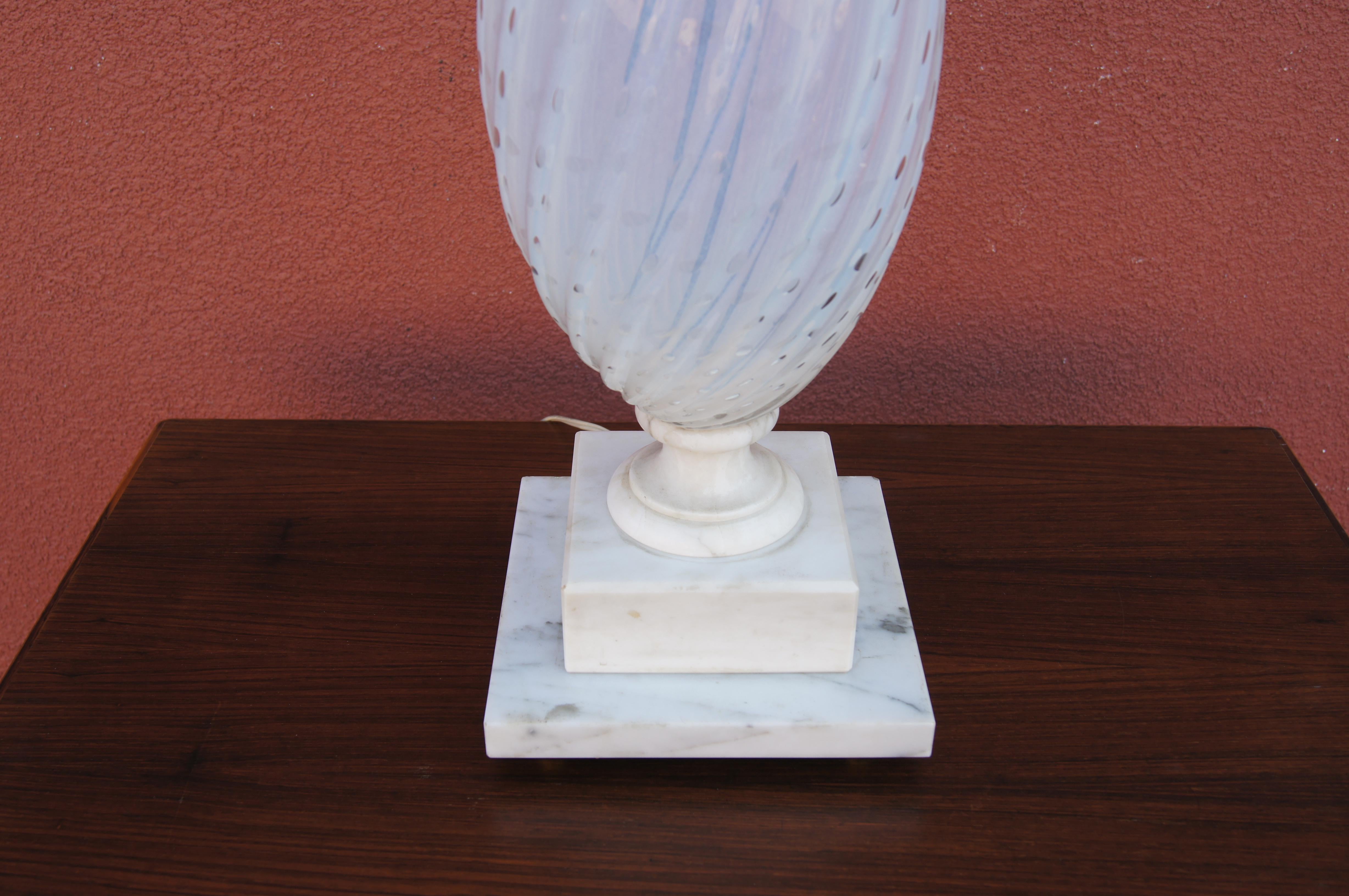 Diese hohe Tischleuchte aus Italien hat eine sanft gedrehte Tropfenform aus mundgeblasenem weißem Muranoglas, die auf einem klassischen quadratischen Marmorsockel steht.

Die unten angegebenen Maße beziehen sich auf die Oberseite des