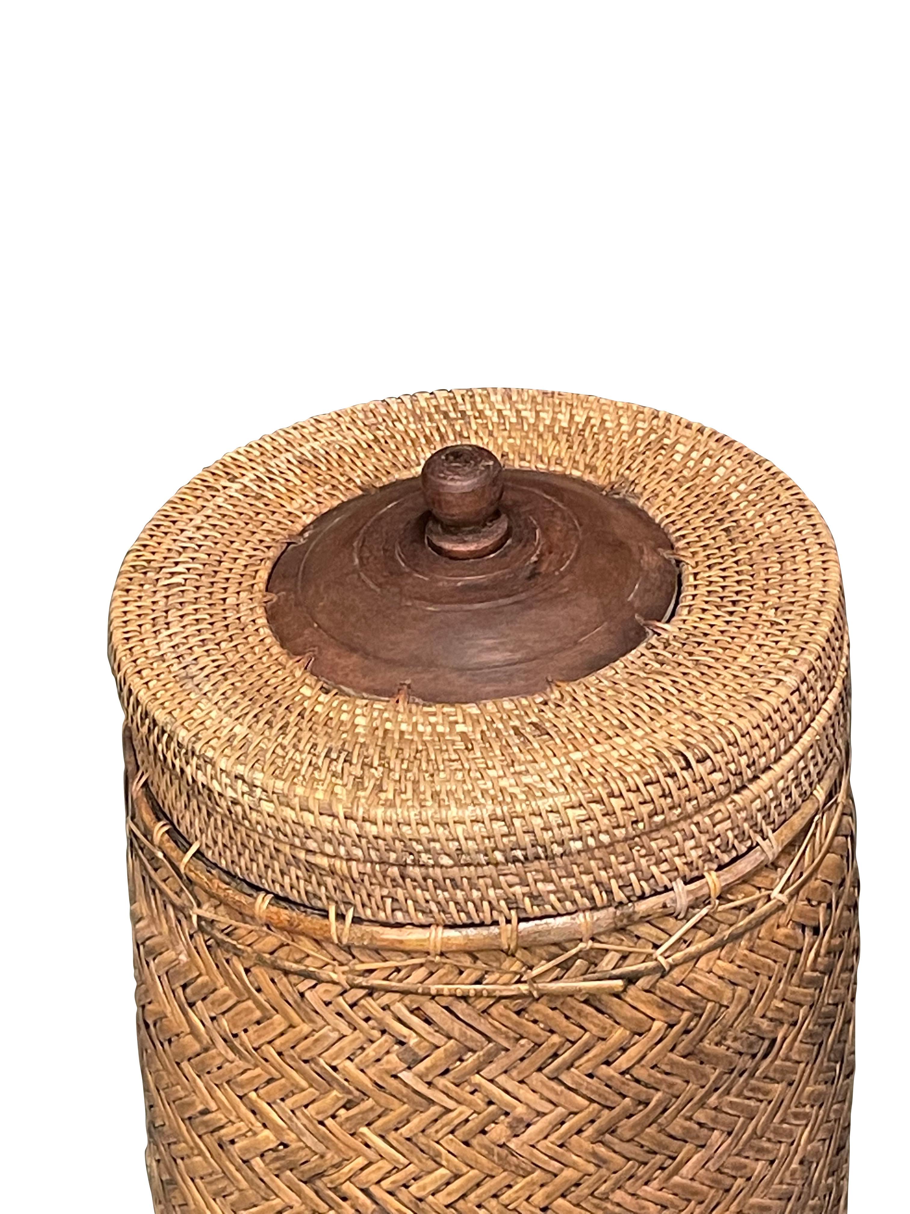 Contemporary Indonesian tall woven wicker lidded basket.
Chevron pattern on body and alternate design on top.
Metal pull knob.
Basket sits on square wooden base for support.

