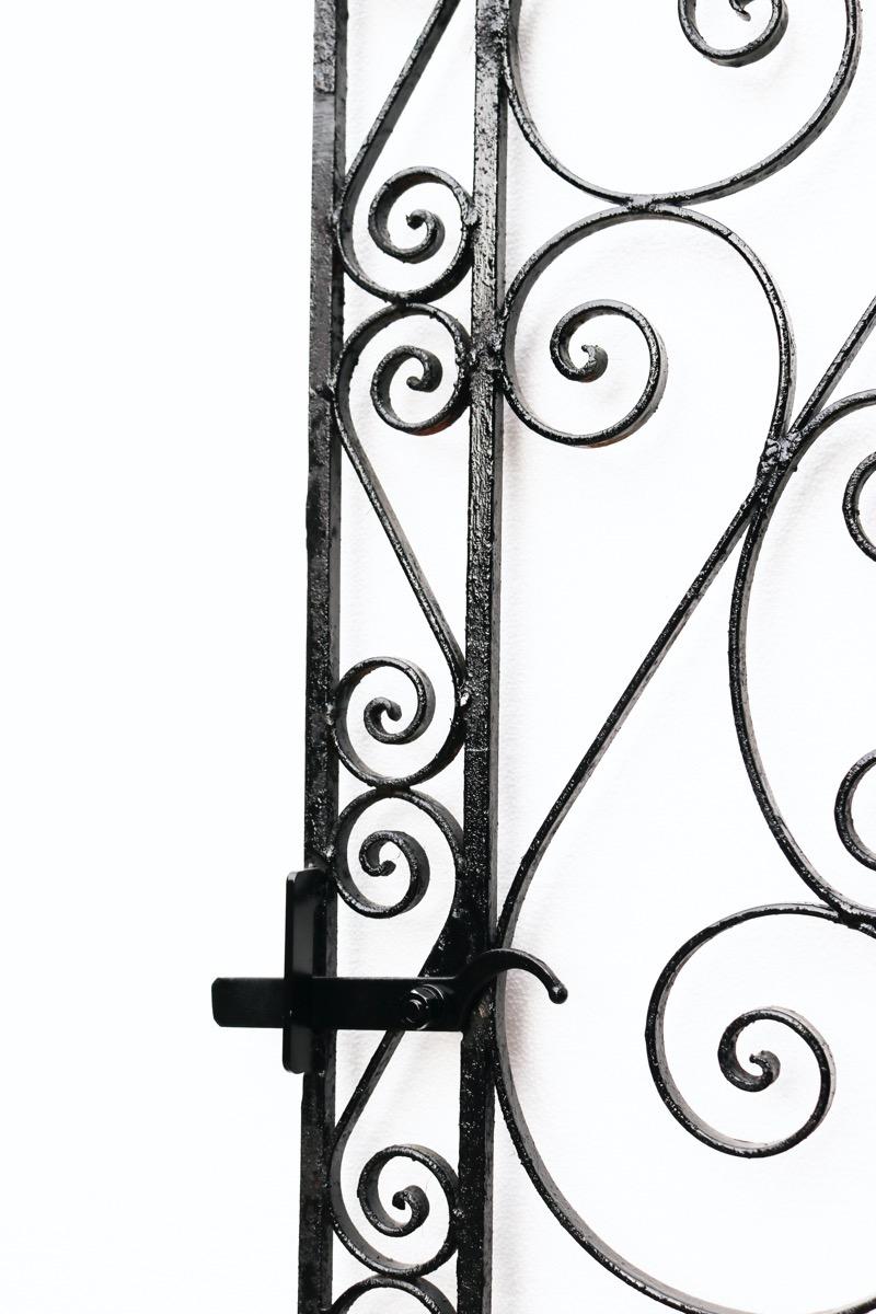 A tall and slender garden gate with a repeated scrolling design.
