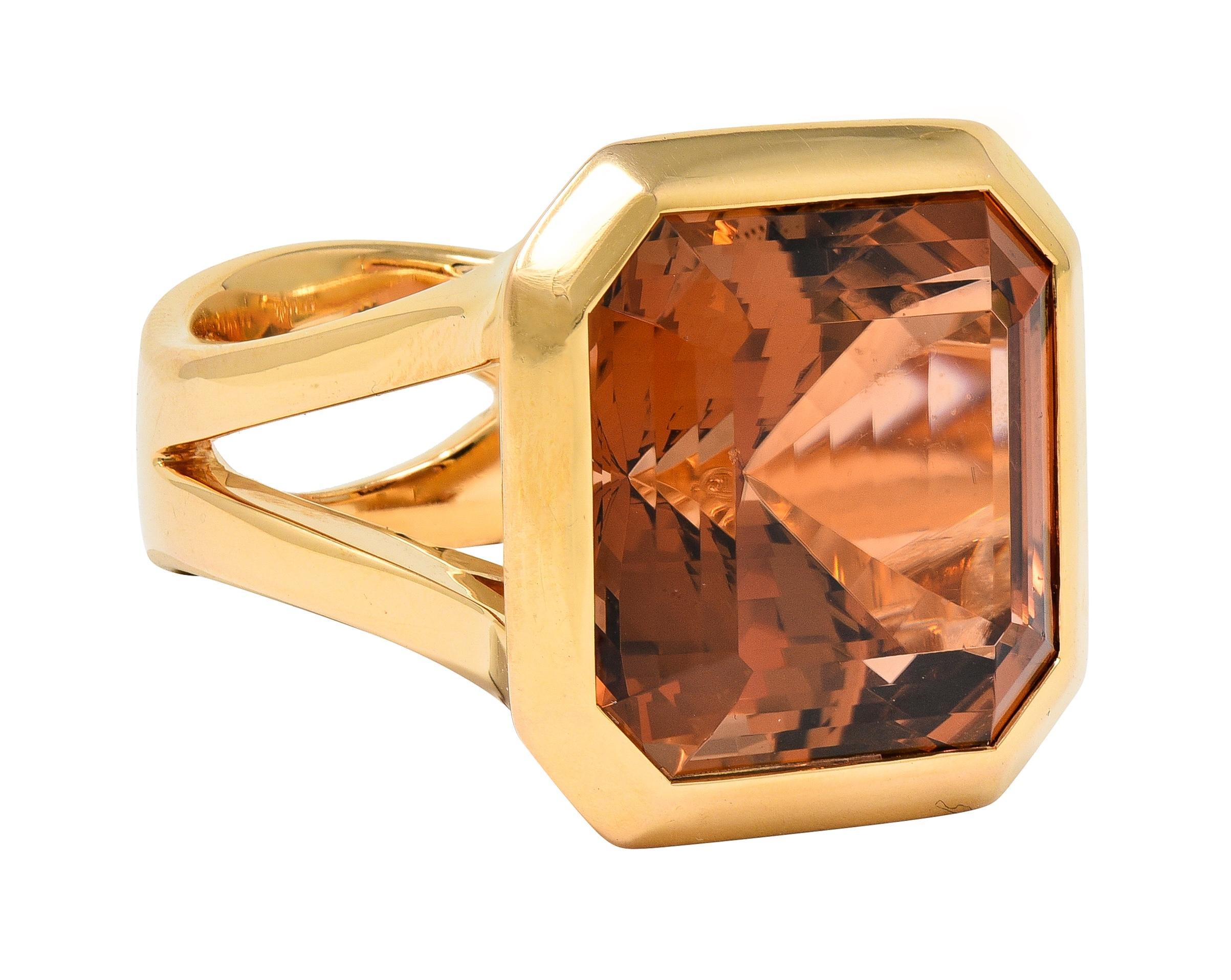 Centering a square step-cut tourmaline weighing approximately 27.95 carats 
Natural with no indications of treatment - transparent brownish orange in color
Bezel set and flanked by split shoulders with chevron profile 
Completed by shank pierced