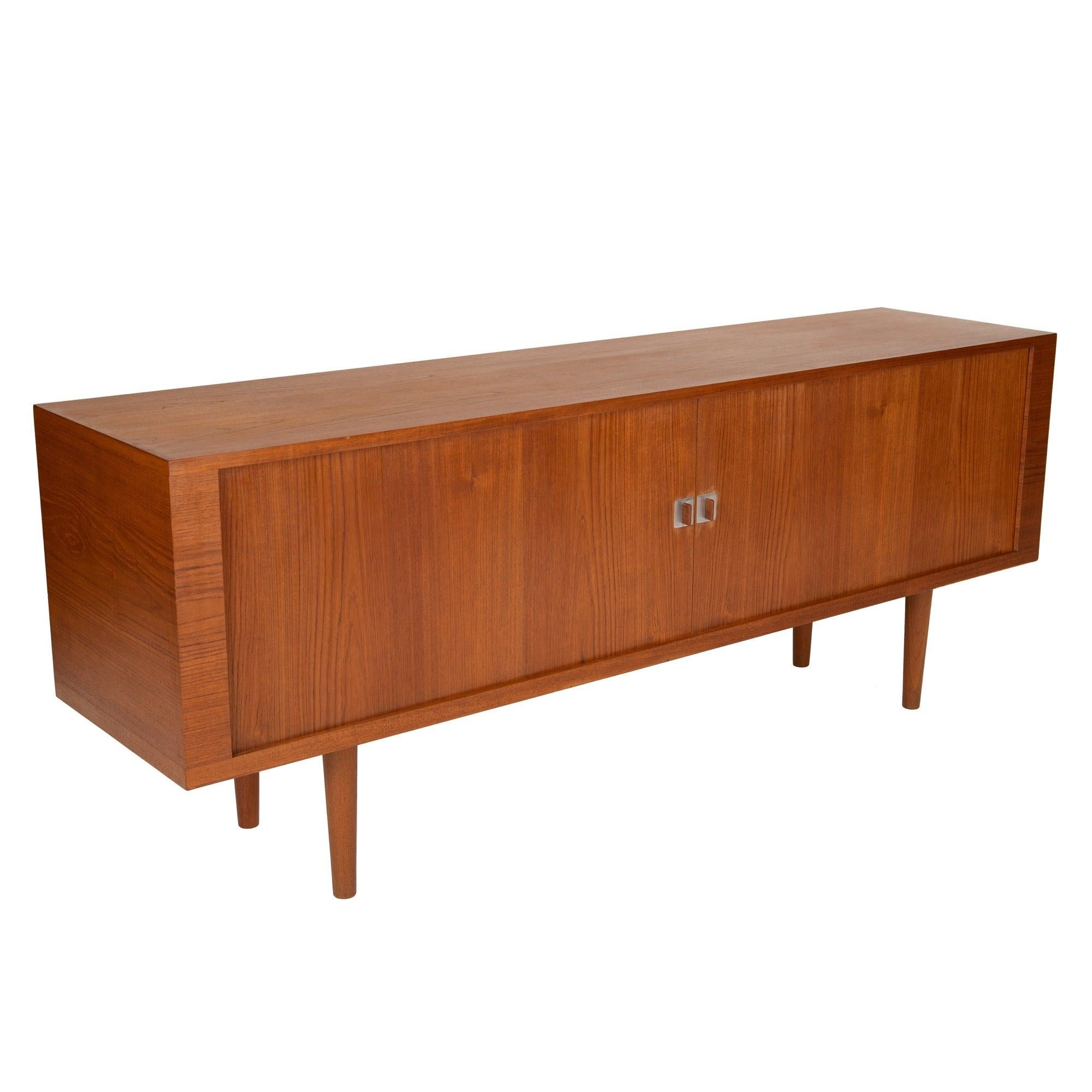 A credenza in warm teak with tambour doors, sculpted tab pulls, turned dowel legs and three divided storage compartments.