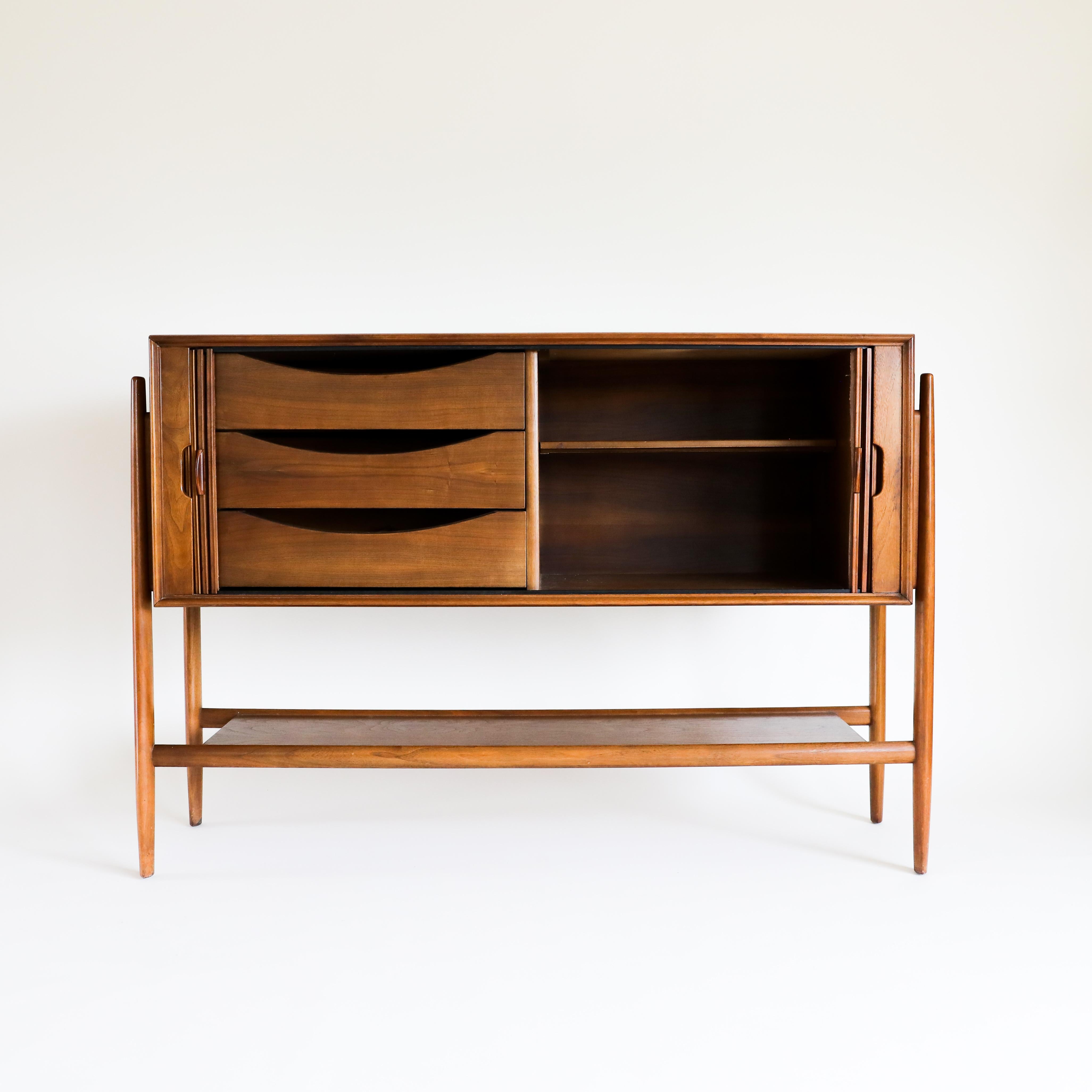 A rare and exceptional Mid-Century Modern walnut tambour door sideboard or credenza designed by Barney Flagg for the Parallel line by Drexel. The credenza features gorgeous walnut wood grain and sleek exoskeletal legs and the honey golden hue that
