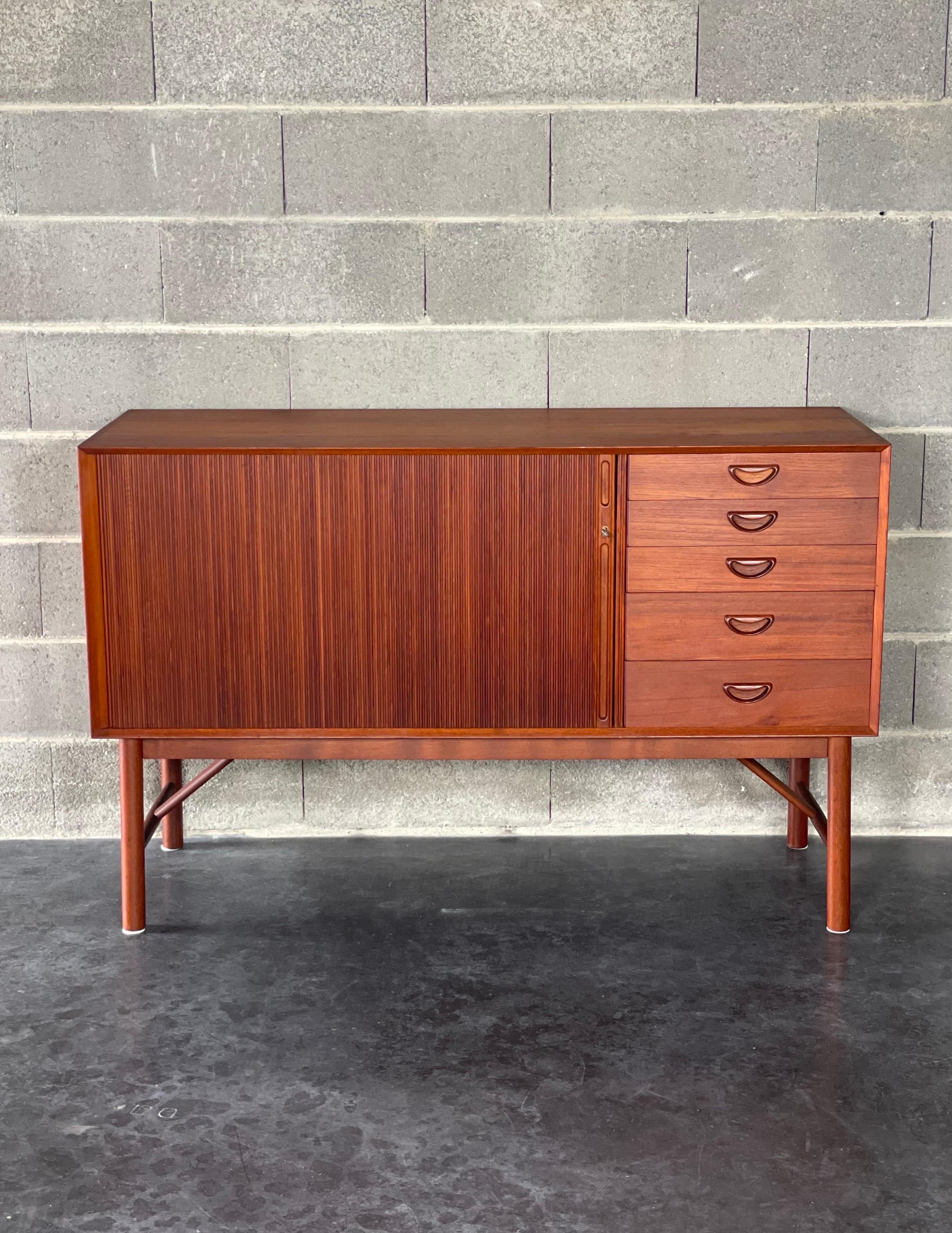 A rare sideboard by Peter Hvidt & Orla Mølgaard Nielsen, Made in Denmark in 1958 by Søborg Møbler. Features a high quality crafting in solid teak wood with finger- jointed case a lockable tambour door and five drawers.