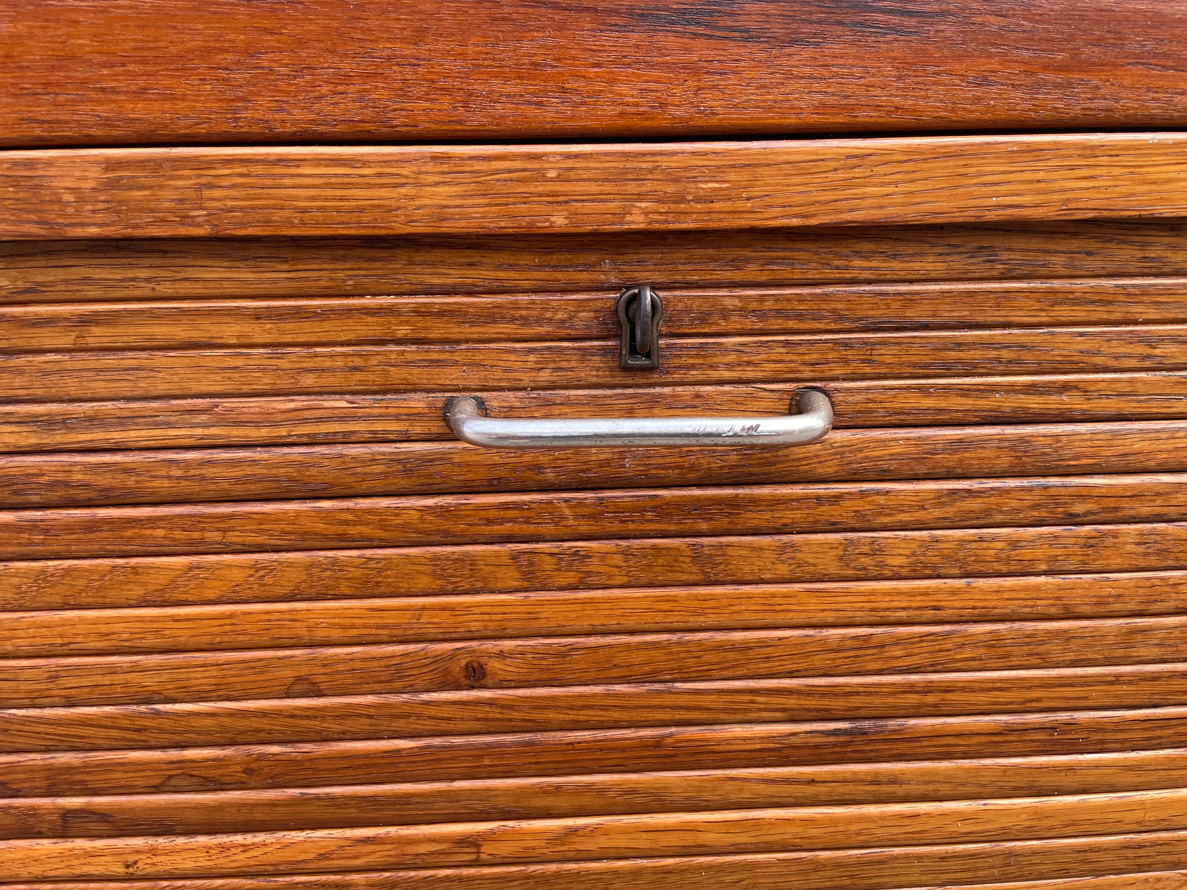 A simple storage cabinet with a finely slatted tambour front that conceals adjustable shelves and file storage, for the Aarhus City Hall, Denmark 1941.