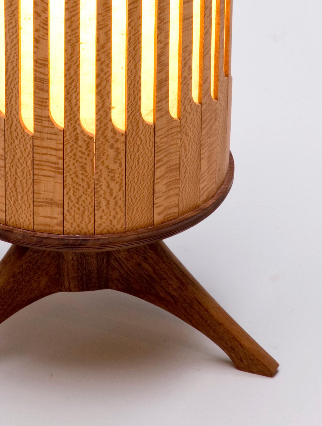 This lamp is an experiment in form and construction. The lacewood slats that make up the shade are constructed similarly to the tambours of a roll top desk but are repurposed to surround a light source. The paper lining softens the light to create