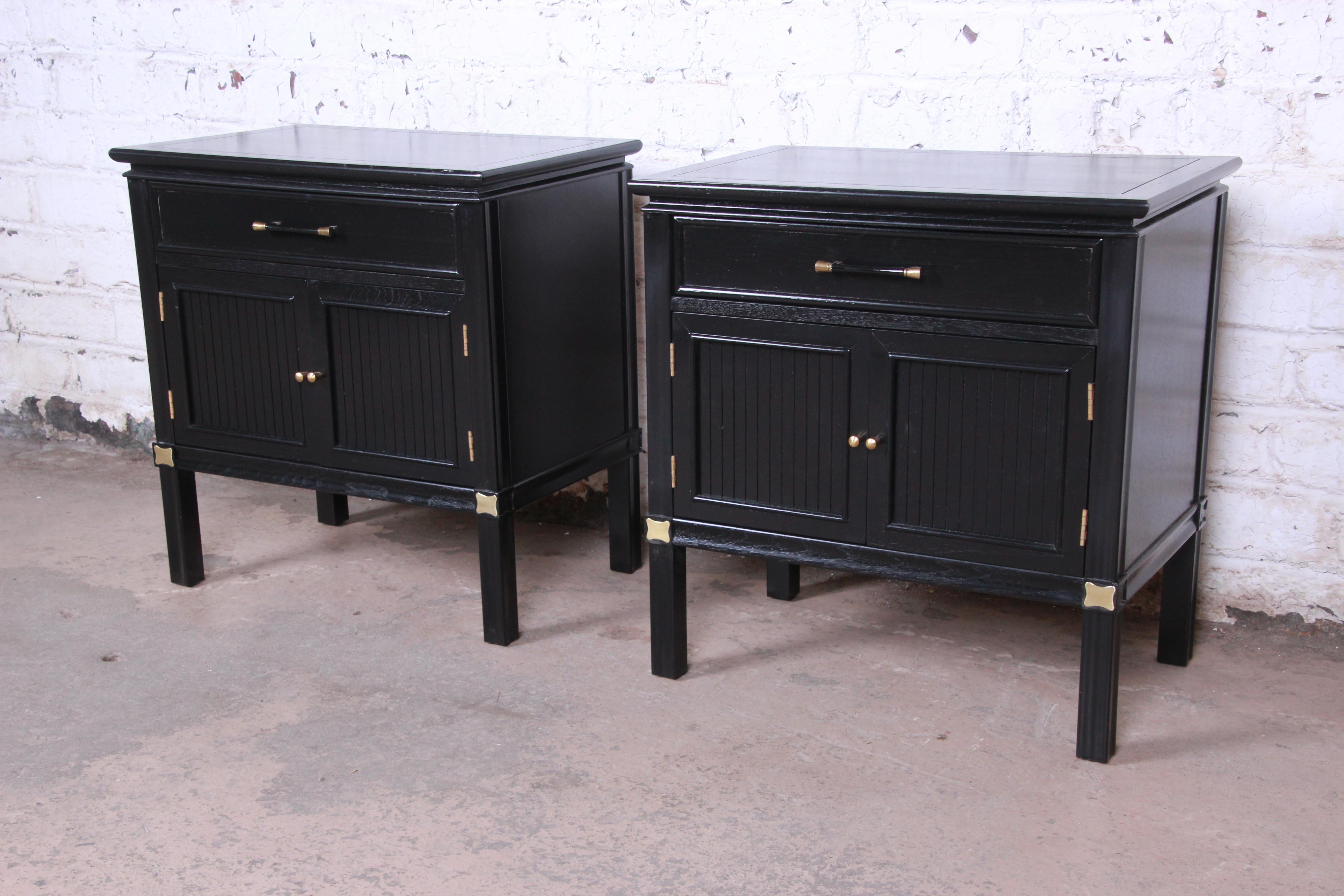 An exceptional pair of Hollywood Regency chinoiserie nightstands or end tables from the Tamerlane Collection by Thomasville. The nightstands feature gorgeous walnut wood grain with a newly ebonized finish and brass hardware and accents. They offer