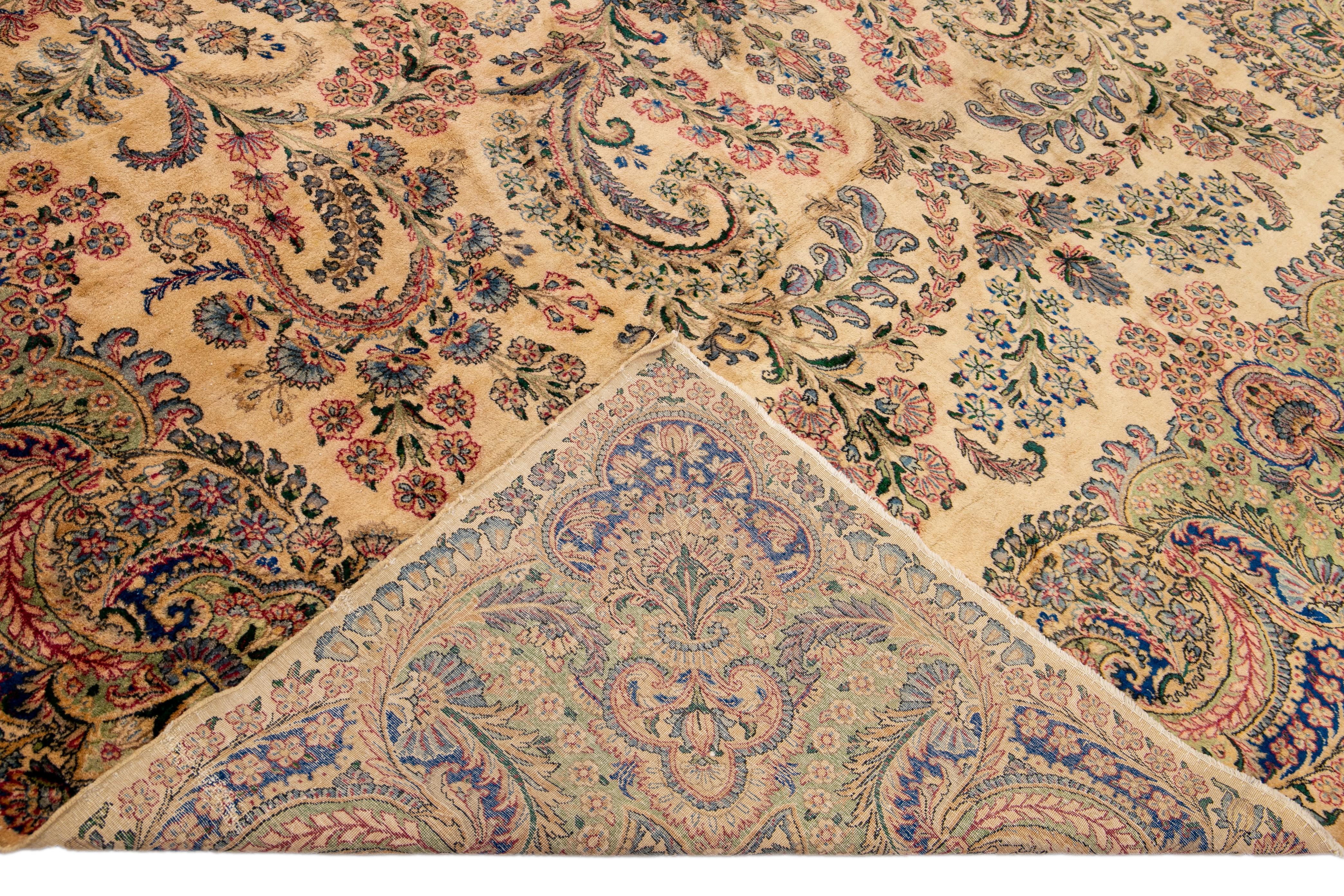 Beautiful Antique Kerman hand-knotted wool rug with the beige field. This Persian rug has a designed frame and blue, red, and green accents in a gorgeous all-over botanical floral design. 

This rug measures: 9'8
