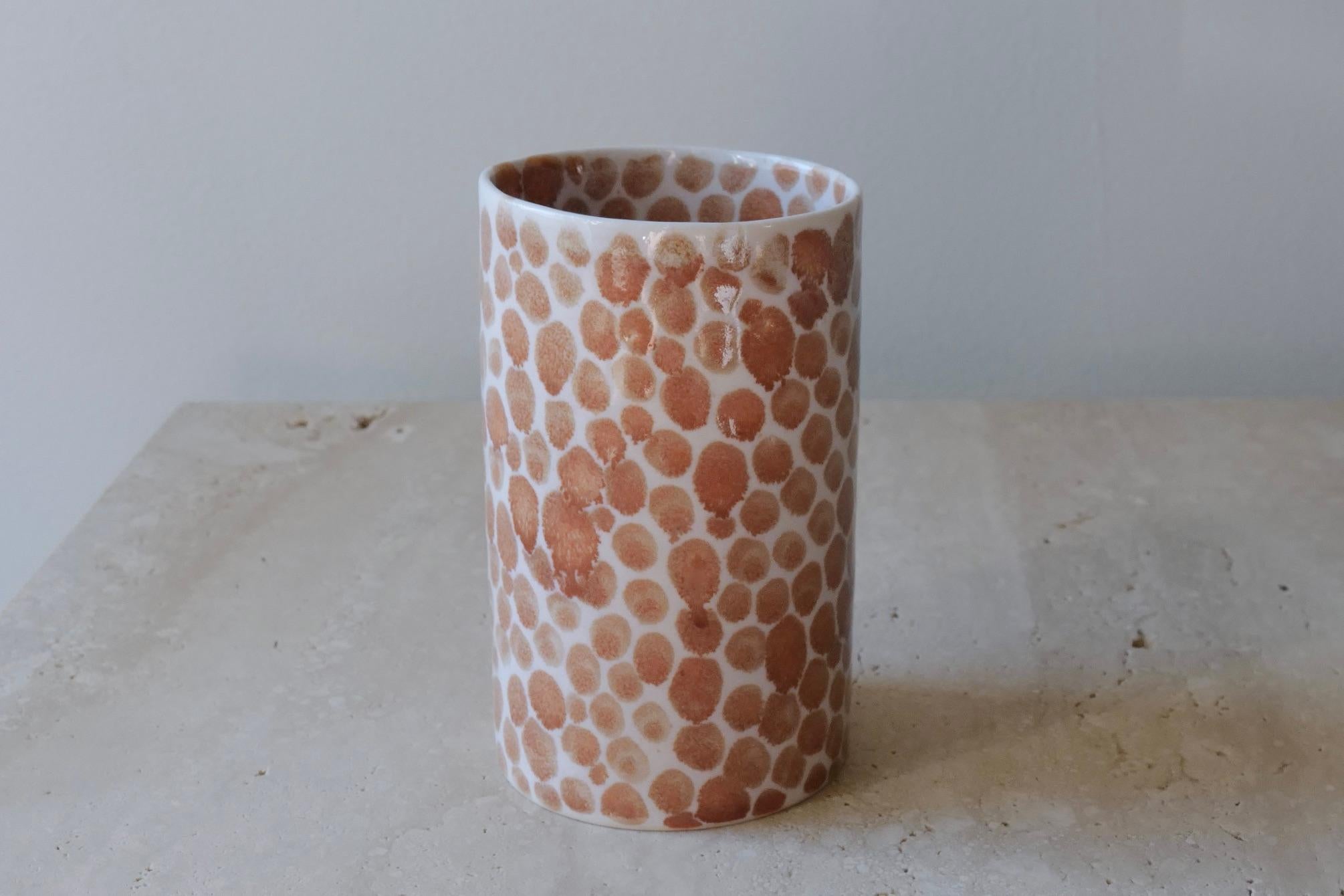 Ceramic drinking cup. Hand-cast in porcelain and once bisque fired, each dot is hand painted with a tan glaze. An unconventional layered glazing technique, developed by the artist, is used in these cast porcelain pieces. The straight walls and sleek