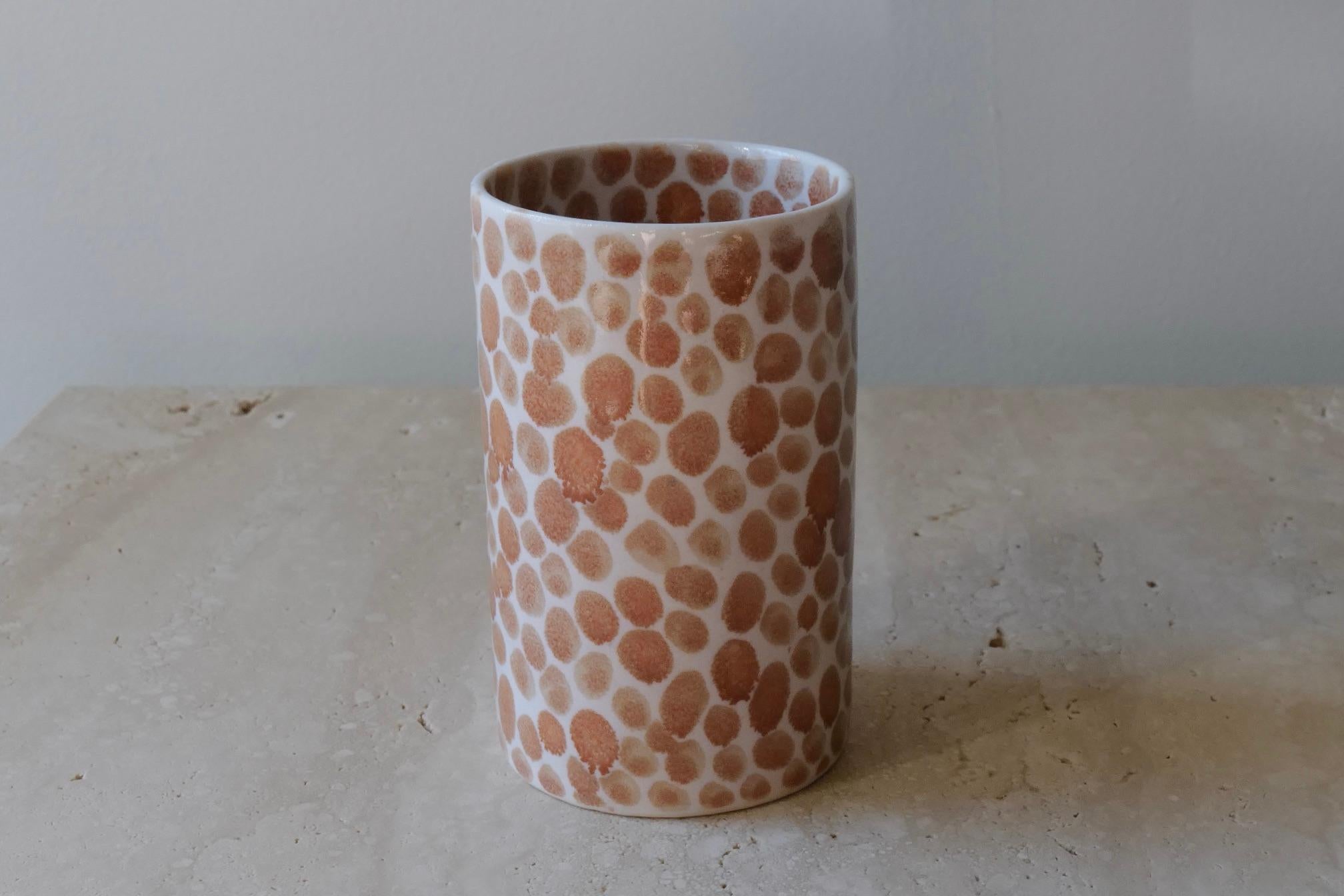Ceramic drinking cup. Hand-cast in porcelain and once bisque fired, each dot is hand-painted with a tan glaze. An unconventional layered glazing technique, developed by the artist, is used in these cast porcelain pieces. The straight walls and sleek
