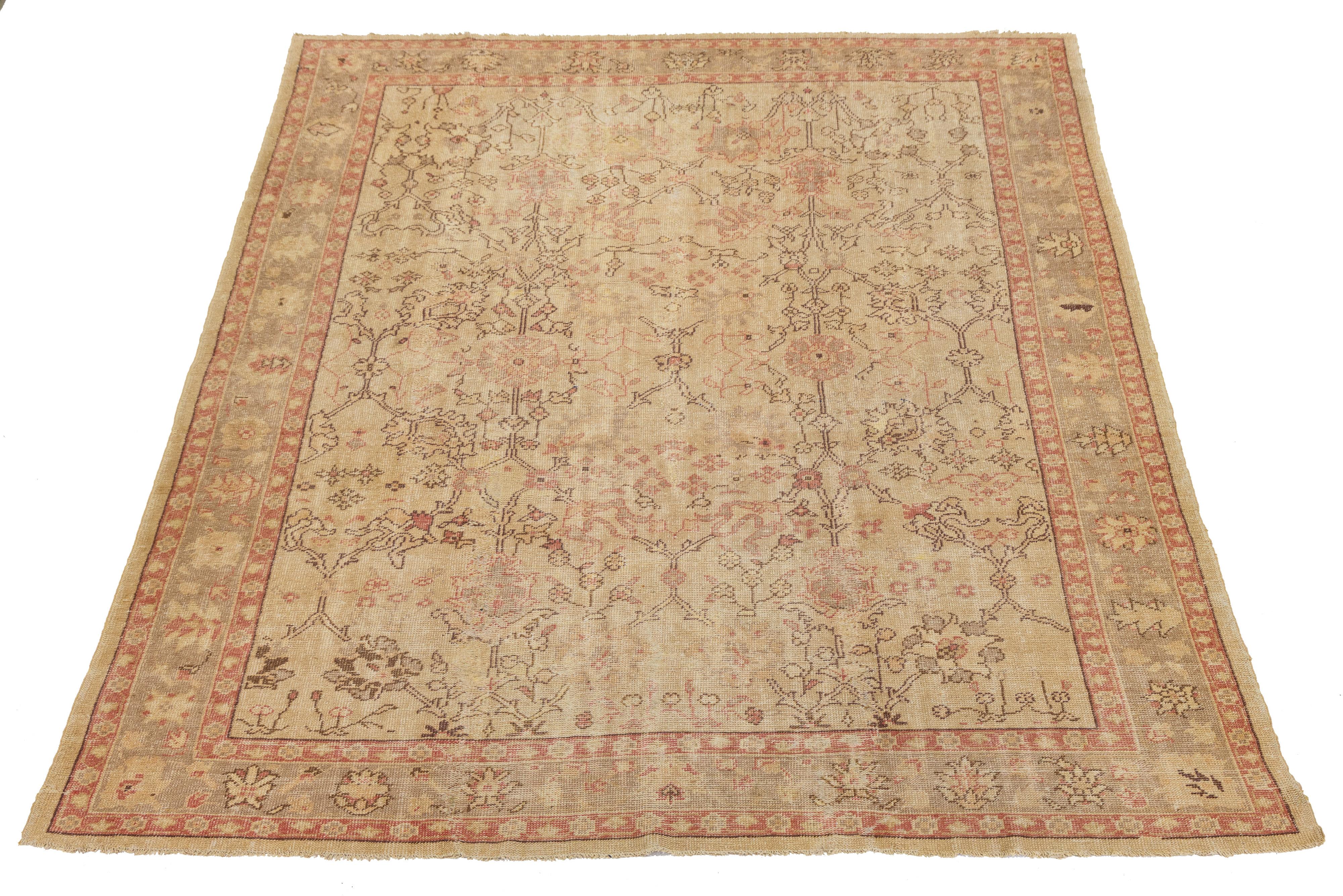 This vintage Turkish Oushak rug is hand-knotted from wool, featuring a neutral tan field complemented by a striking red border. The design prominently displays a floral medallion motif, highlighting the craftsmanship and aesthetic appeal