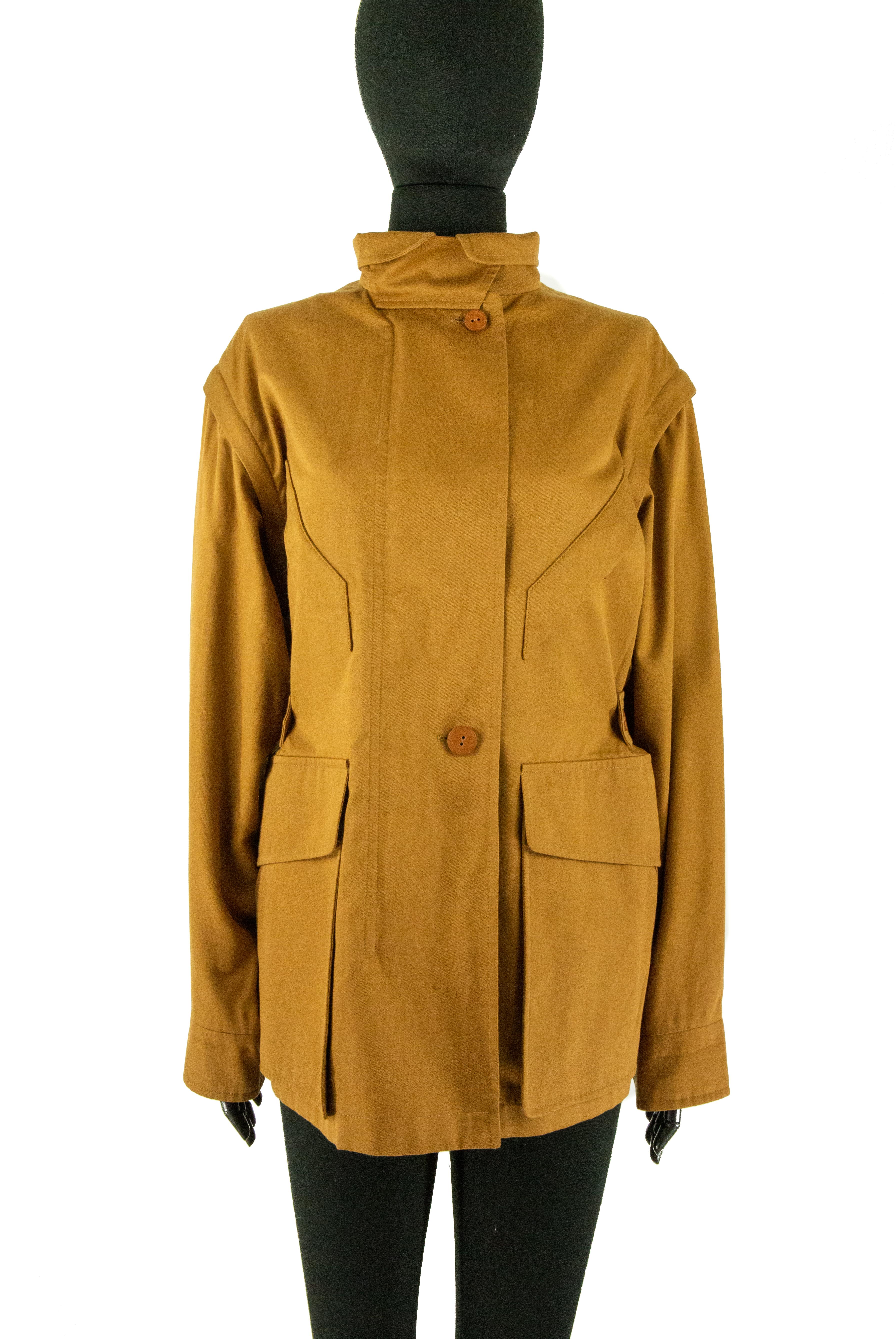 A tan Hermes jacket with detachable sleeves. This cotton jacket features 6 pockets at the front. Two pockets are at the bust of the jacket with a silver zipper and tan leather toggles. The other 4 pockets are in the same location as one another, the